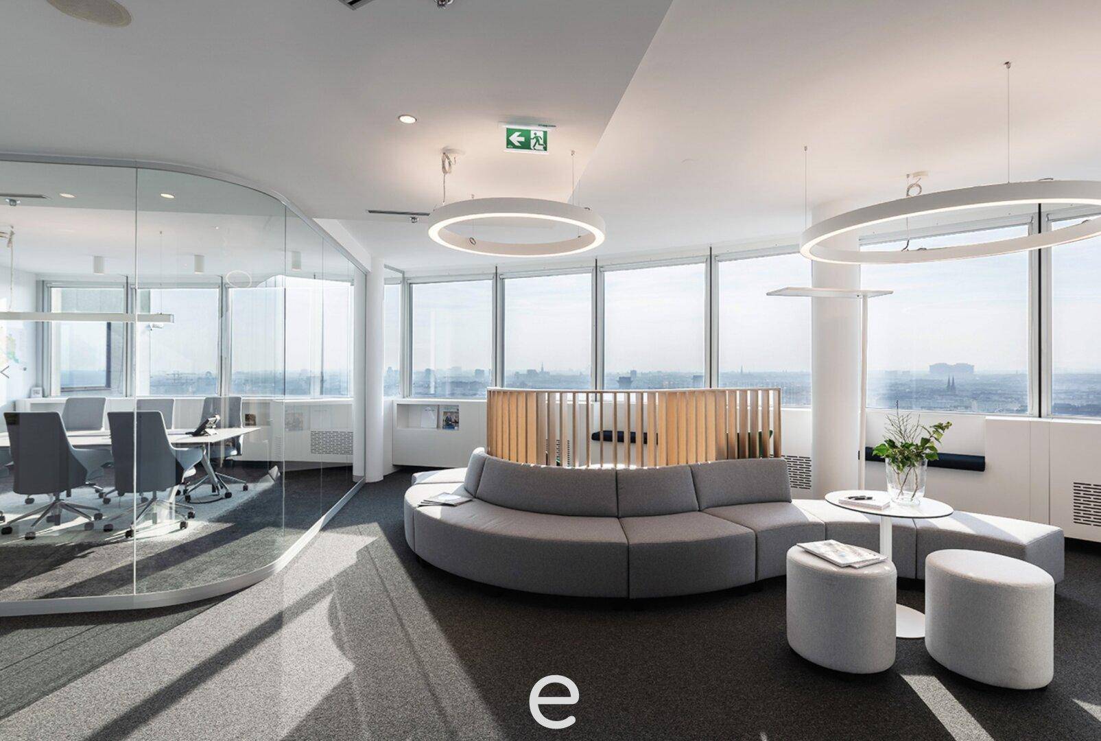 Moderner Bürobereich mit runden Sitzgelegenheiten, Glaswänden und weitem Stadtblick durch große Fenster.