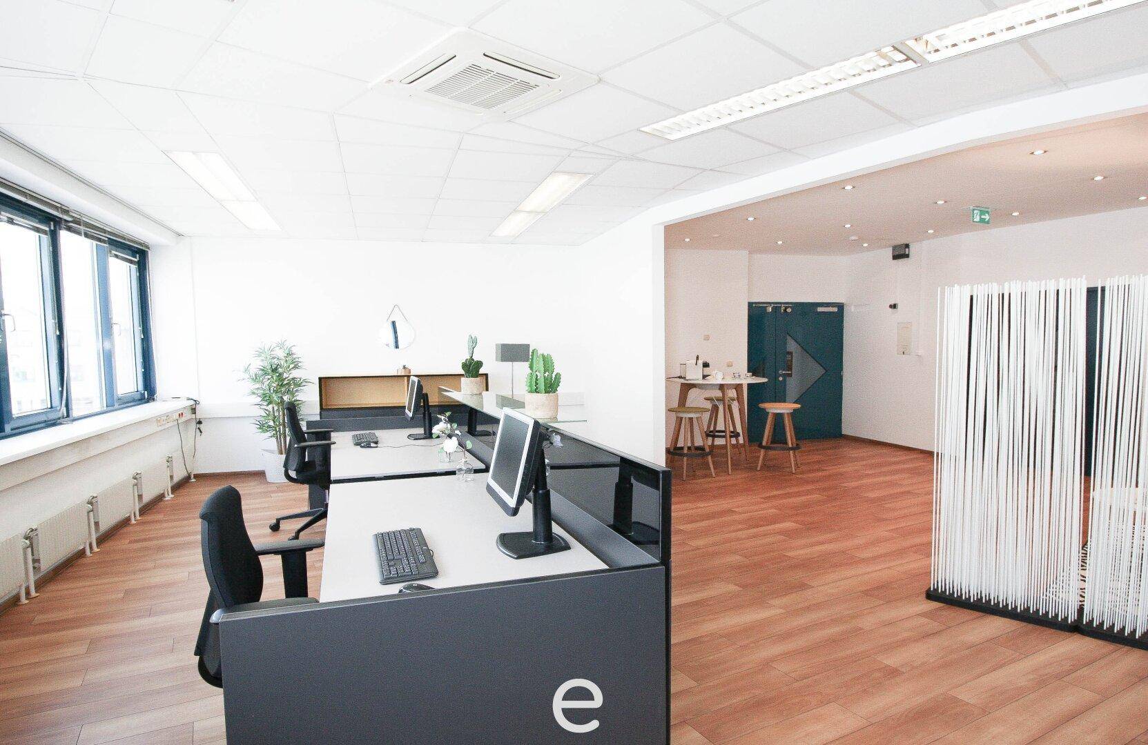 Offener Bürobereich mit mehreren Arbeitsplätzen und Blick auf den Empfangsbereich.