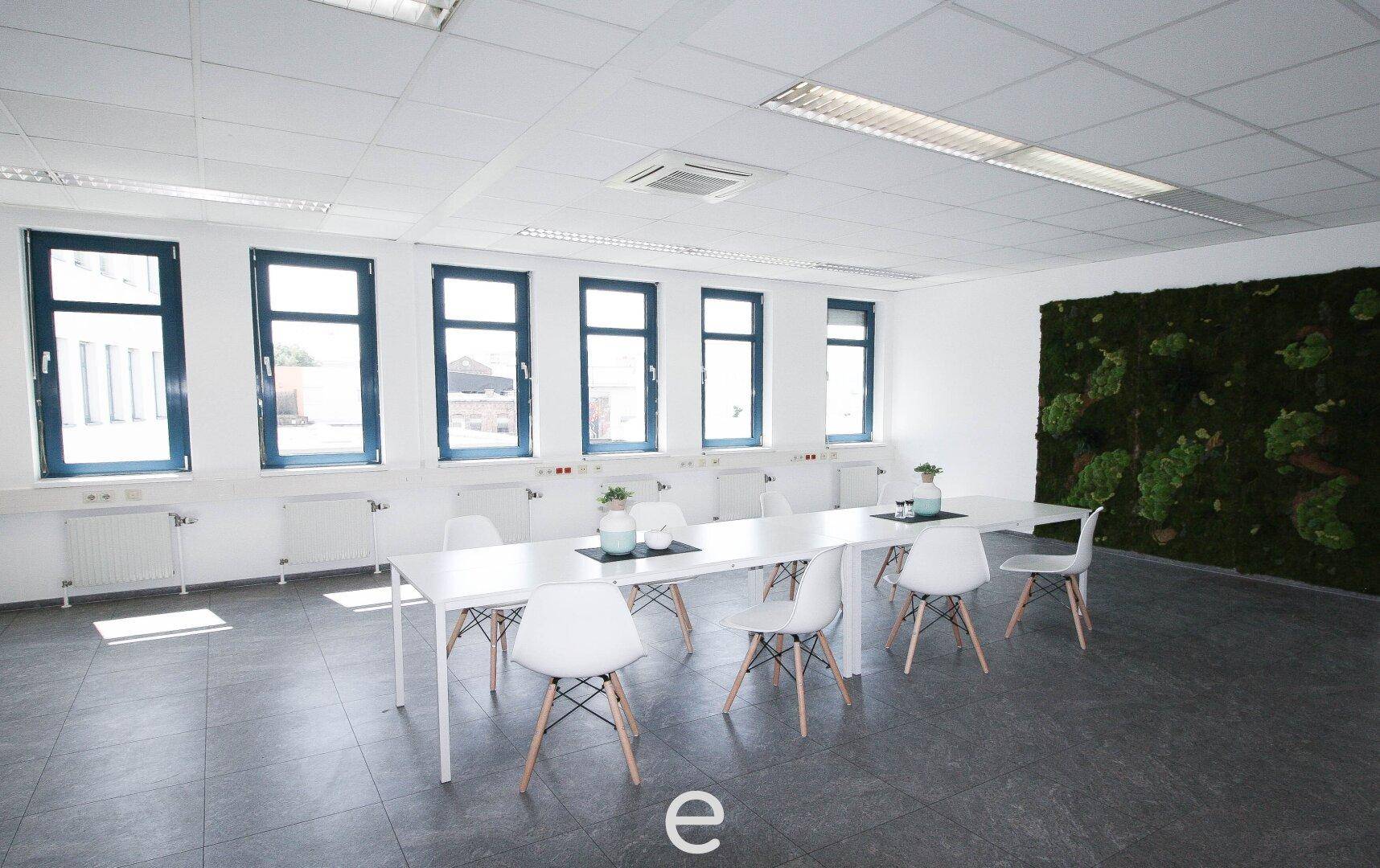 Heller Konferenzraum mit langem Tisch, Stühlen und Mooswand-Dekoration.