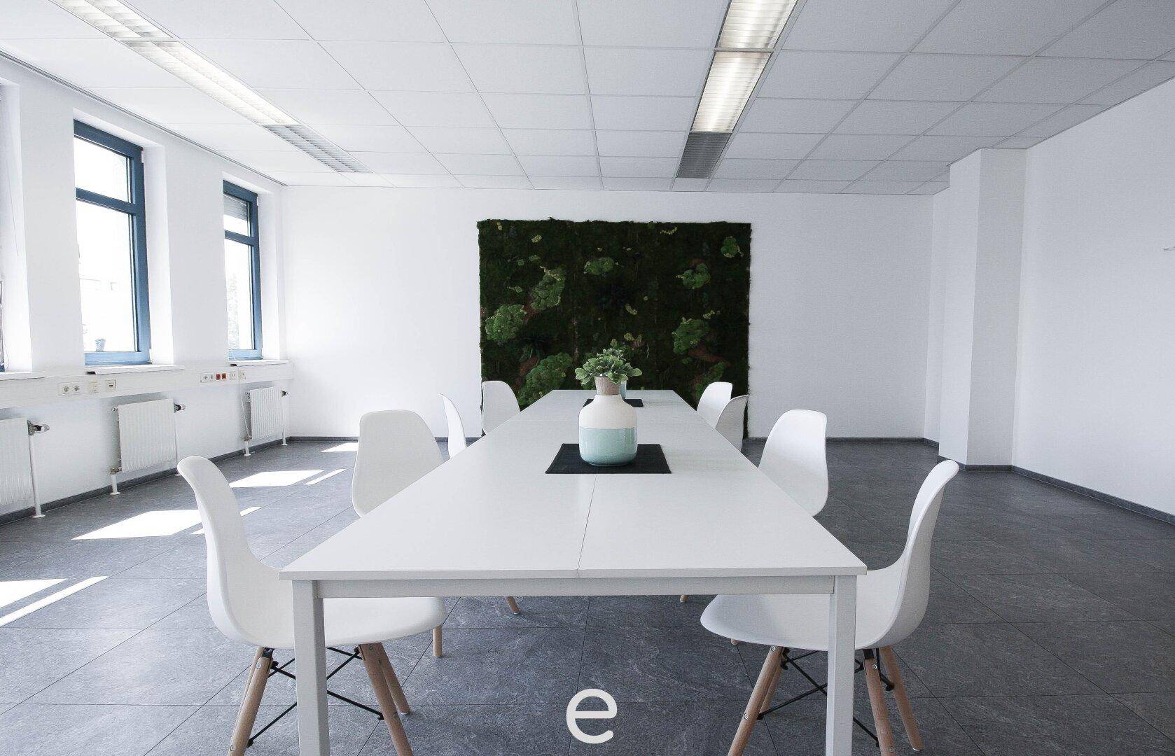 Moderner Konferenzraum mit weißem Tisch, Stühlen und einer großen Mooswand.