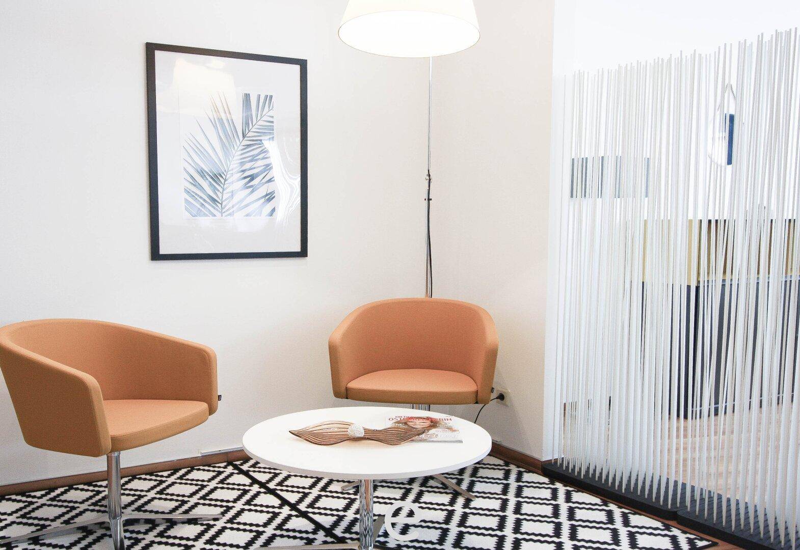 Gemütliche Sitzecke mit zwei orangefarbenen Sesseln, Couchtisch und dekorativem Raumteiler.