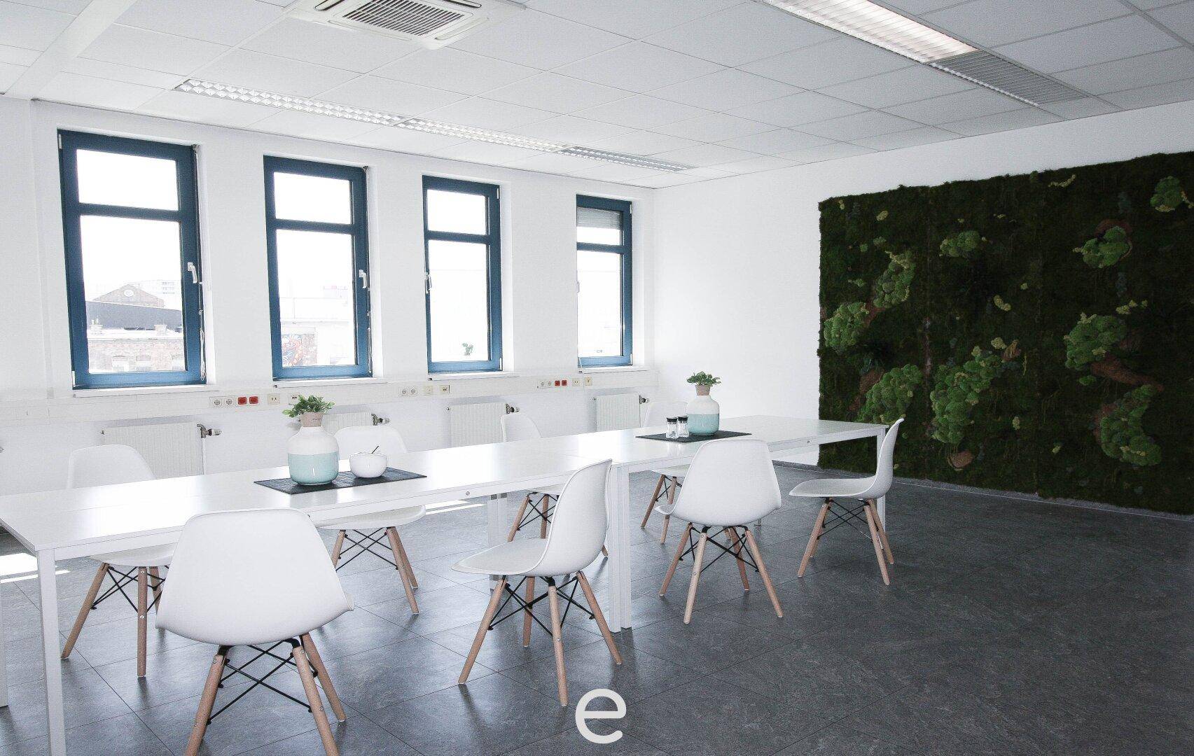 Moderner Konferenzraum mit weißem Tisch, Stühlen und einer großen Mooswand.