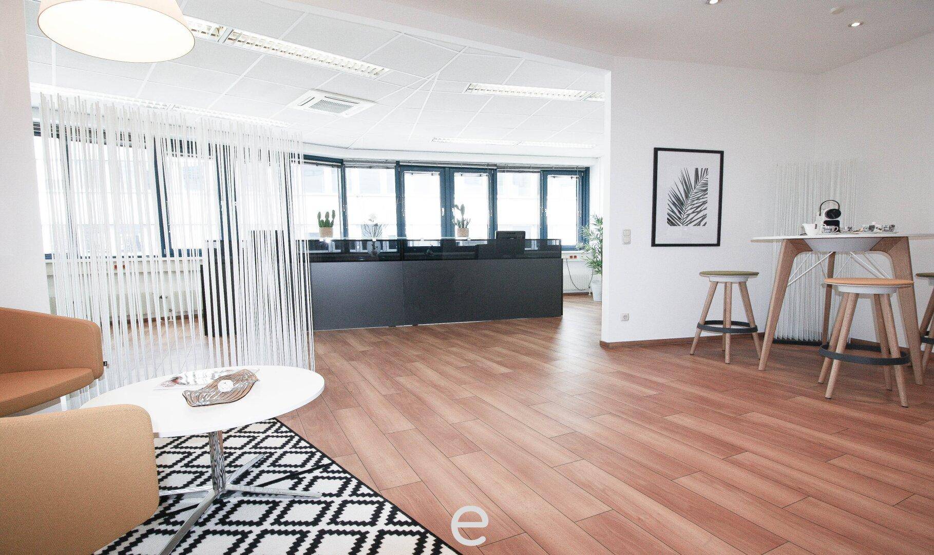 Einladender Empfangsbereich mit Sitzgelegenheiten und einem Blick auf den dahinterliegenden Arbeitsbereich.
