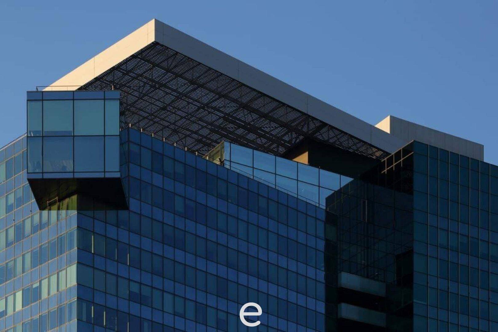Detailaufnahme der oberen Etagen eines modernen Glasturms mit markanter Architektur und blauer Fassade.