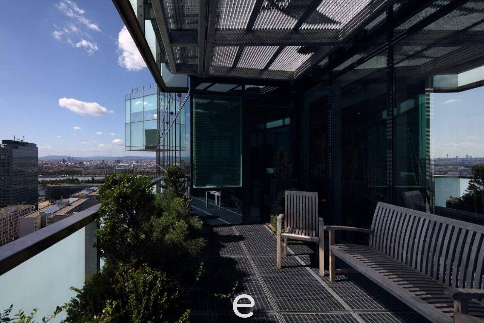 Dachterrasse mit Holzbänken und Pflanzen, die einen weiten Blick über die Stadt und die Umgebung bietet.