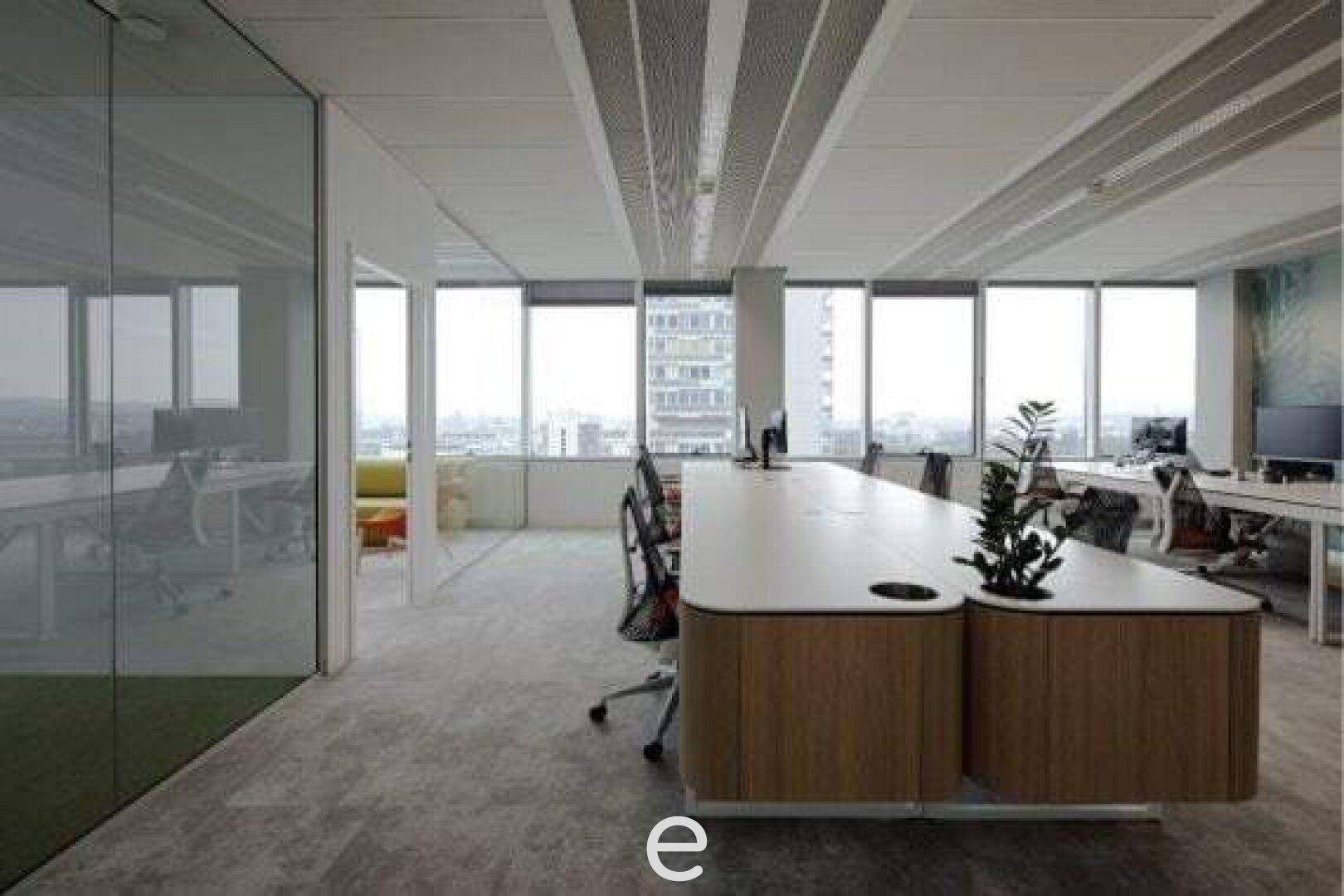 Offener Bürobereich mit modernen Schreibtischen, Glaswänden und weitem Stadtblick durch große Fenster.