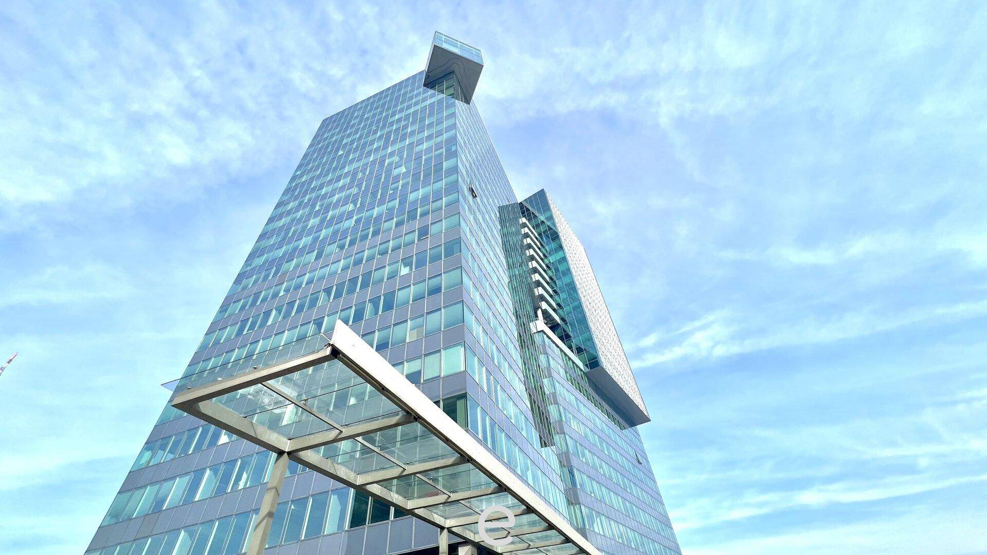 Hohes, modernes Bürogebäude mit blauer Glasfassade unter einem weiten, blauen Himmel.