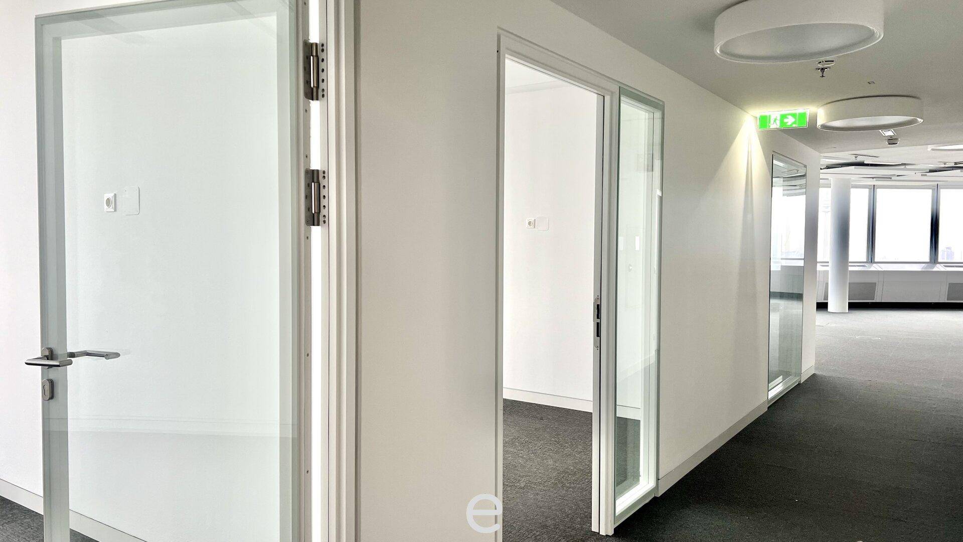 Bürogang mit modernen Glastüren, die zu einzelnen Büroräumen führen, und Teppichboden.