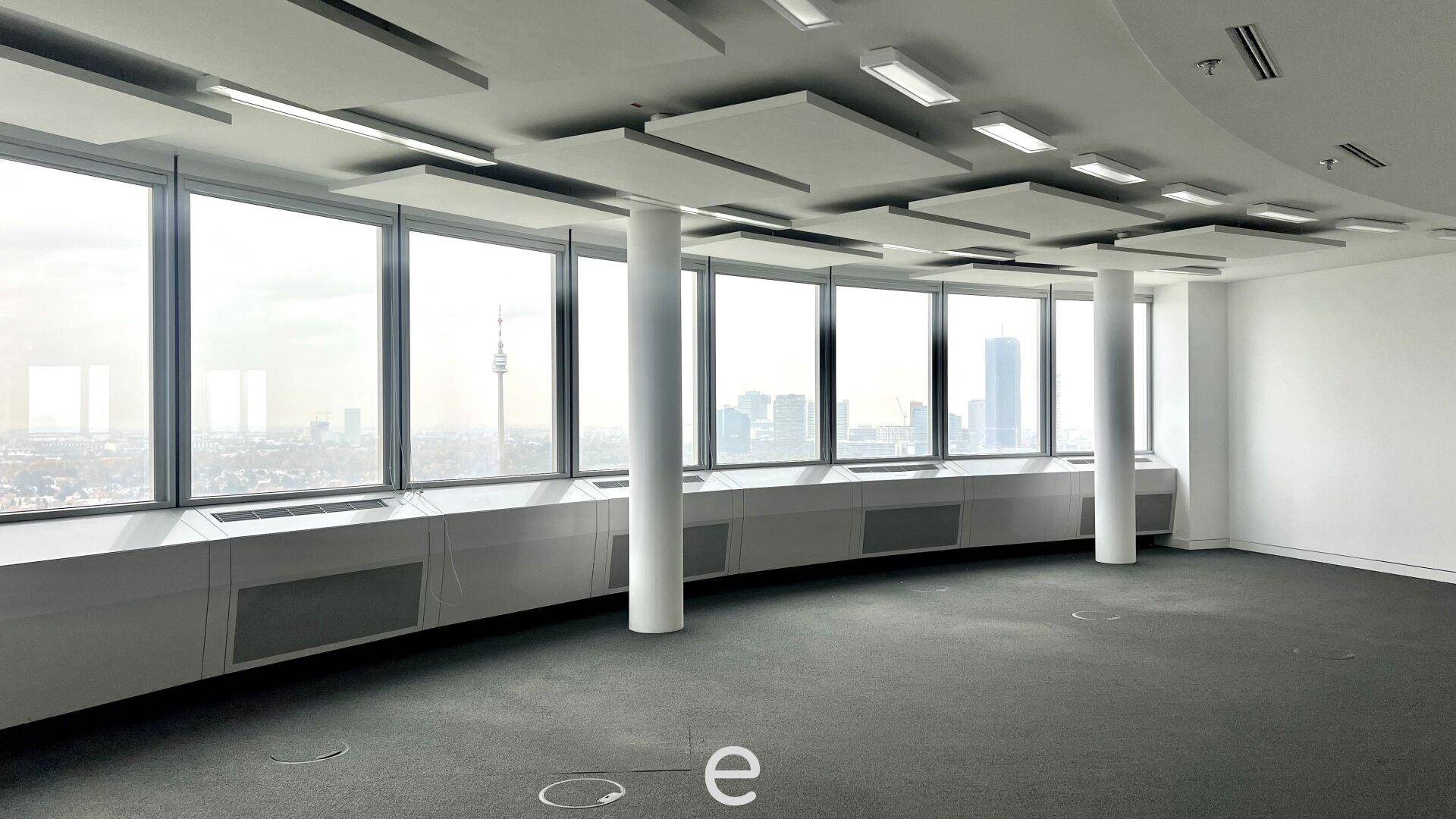 Leerer Büroraum mit geschwungenen Fenstern, die einen Panoramablick auf die Stadt bieten.