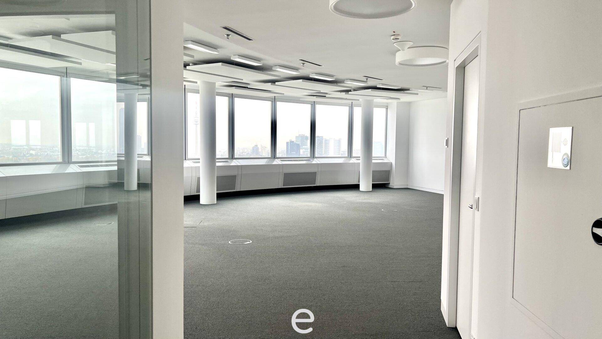 Blick durch eine Tür in einen leeren Büroraum mit großen Fenstern und weitem Stadtblick.