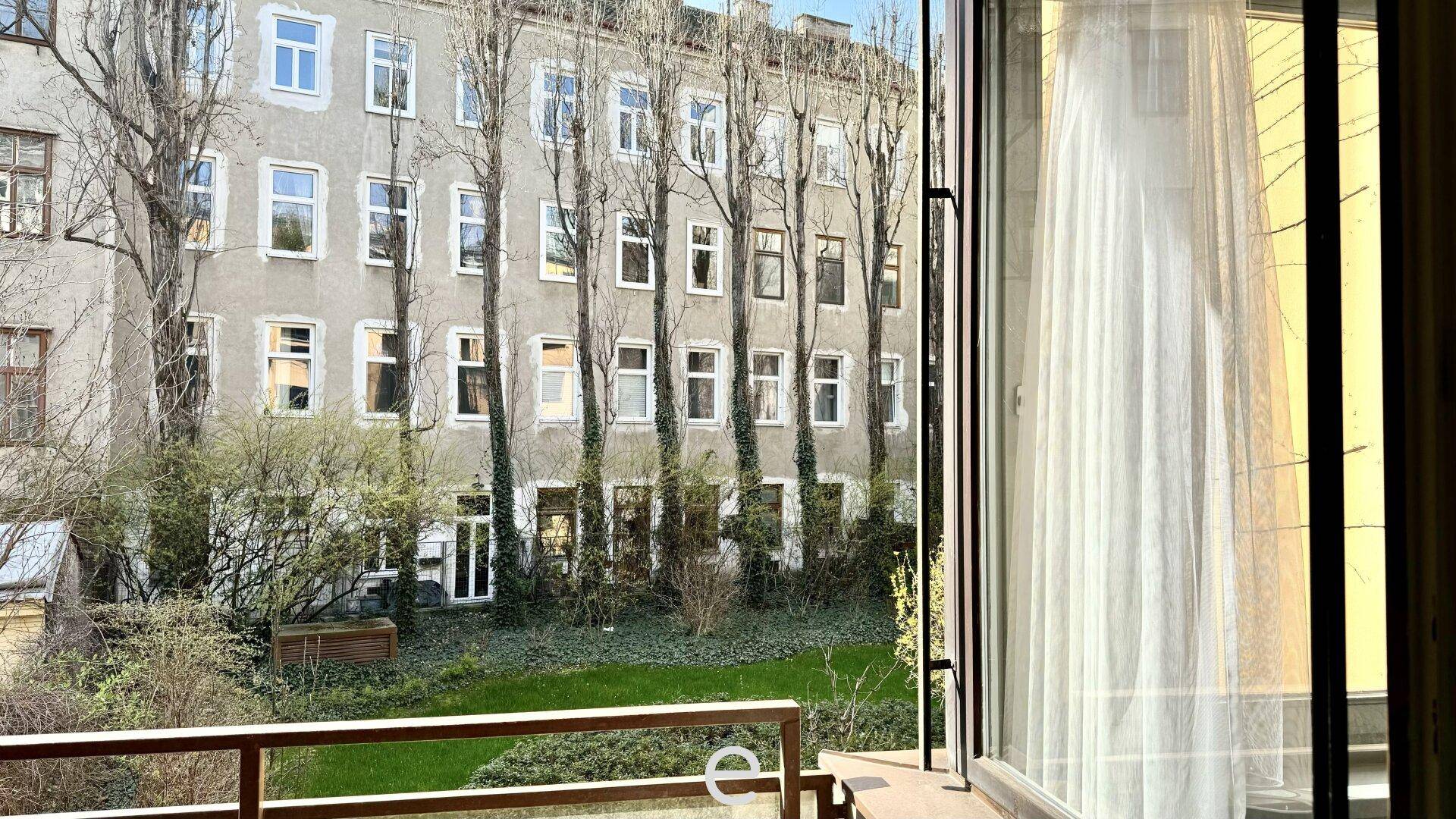 Blick aus dem Fenster auf einen begrünten Innenhof mit Bäumen und einer alten Gebäudefassade.