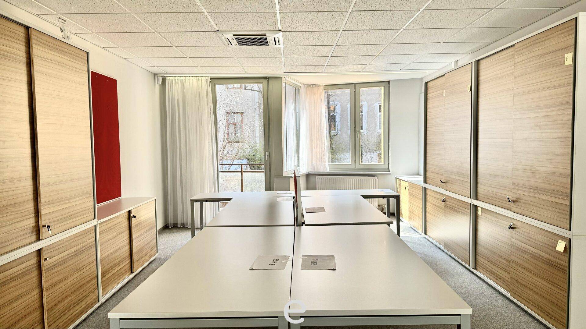 Heller Büroraum mit mehreren Arbeitsplätzen und integrierten Holzschränken für effizienten Stauraum.