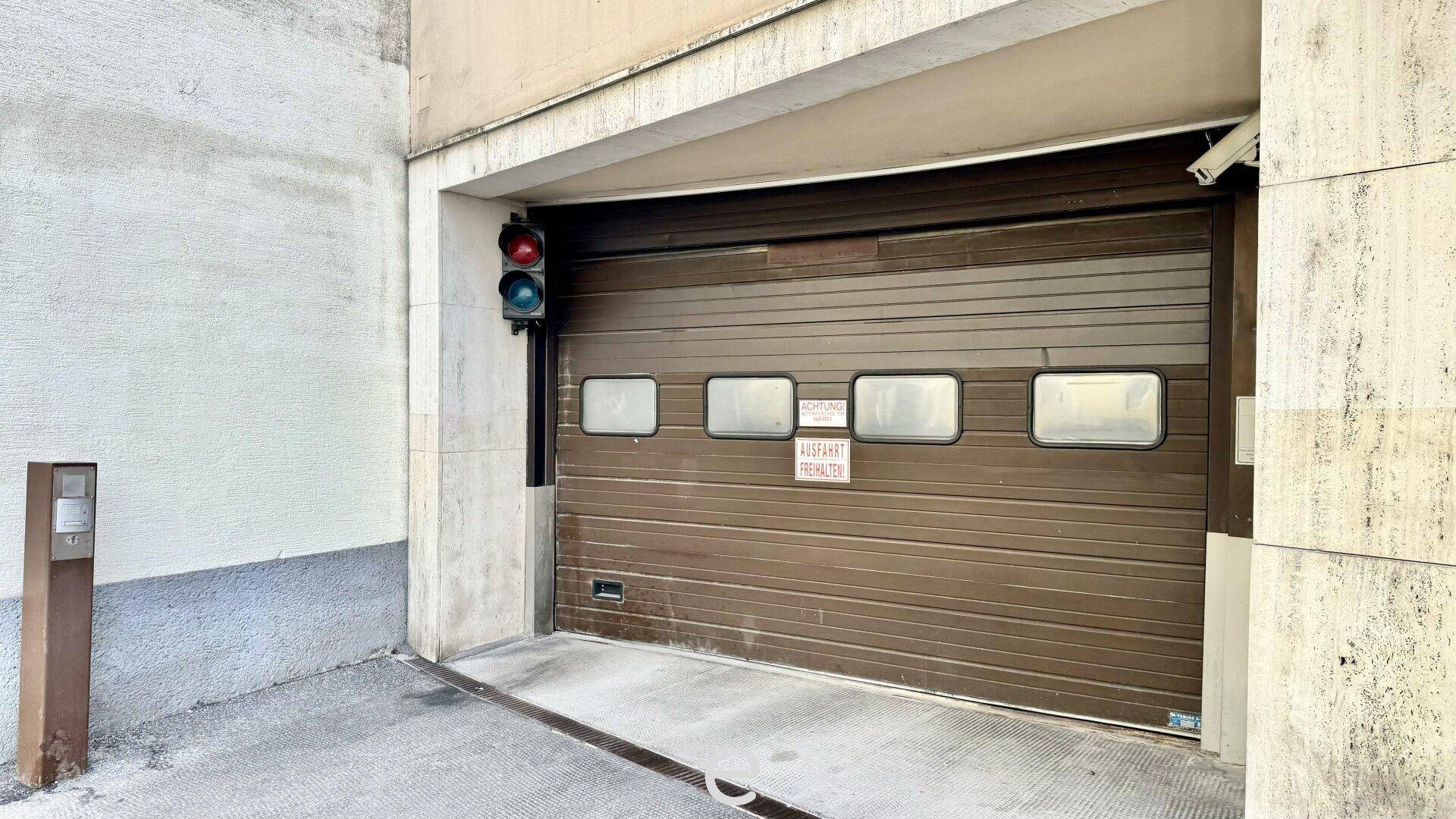 Einfahrt zu einer Tiefgarage mit braunem Rolltor und einer Ampel zur Verkehrsregelung.