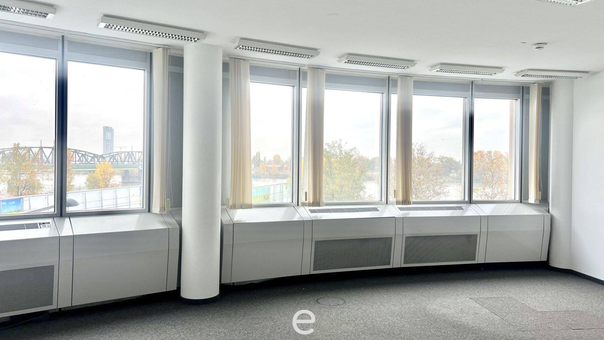 Helles Büro mit Panoramablick auf die Stadt und den Fluss, ausgestattet mit Teppichboden und großen Fenstern.