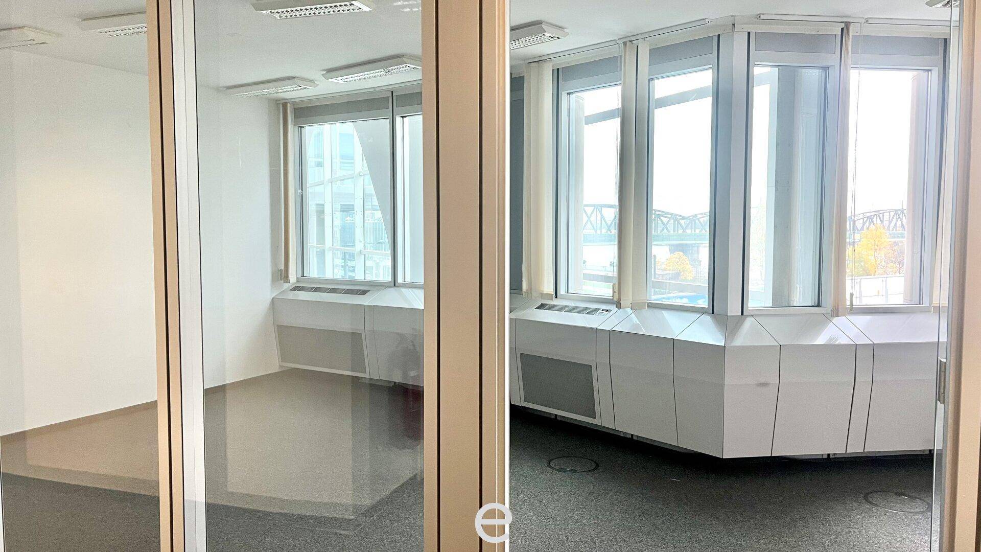 Büro mit Teppichboden und großen Fenstern, die einen Blick auf die Umgebung ermöglichen.