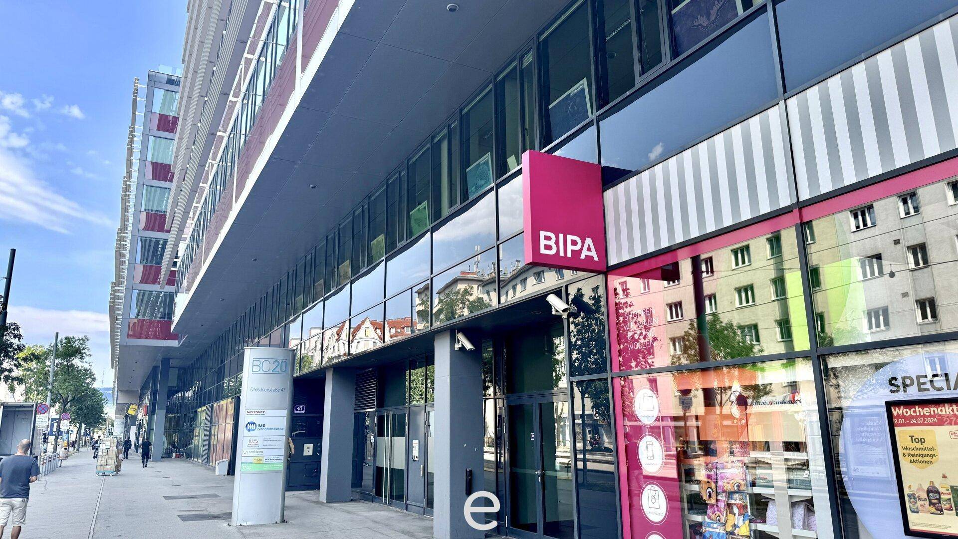 Moderner Eingangsbereich eines Bürogebäudes mit Glasfassade und Geschäftsflächen im Erdgeschoss.