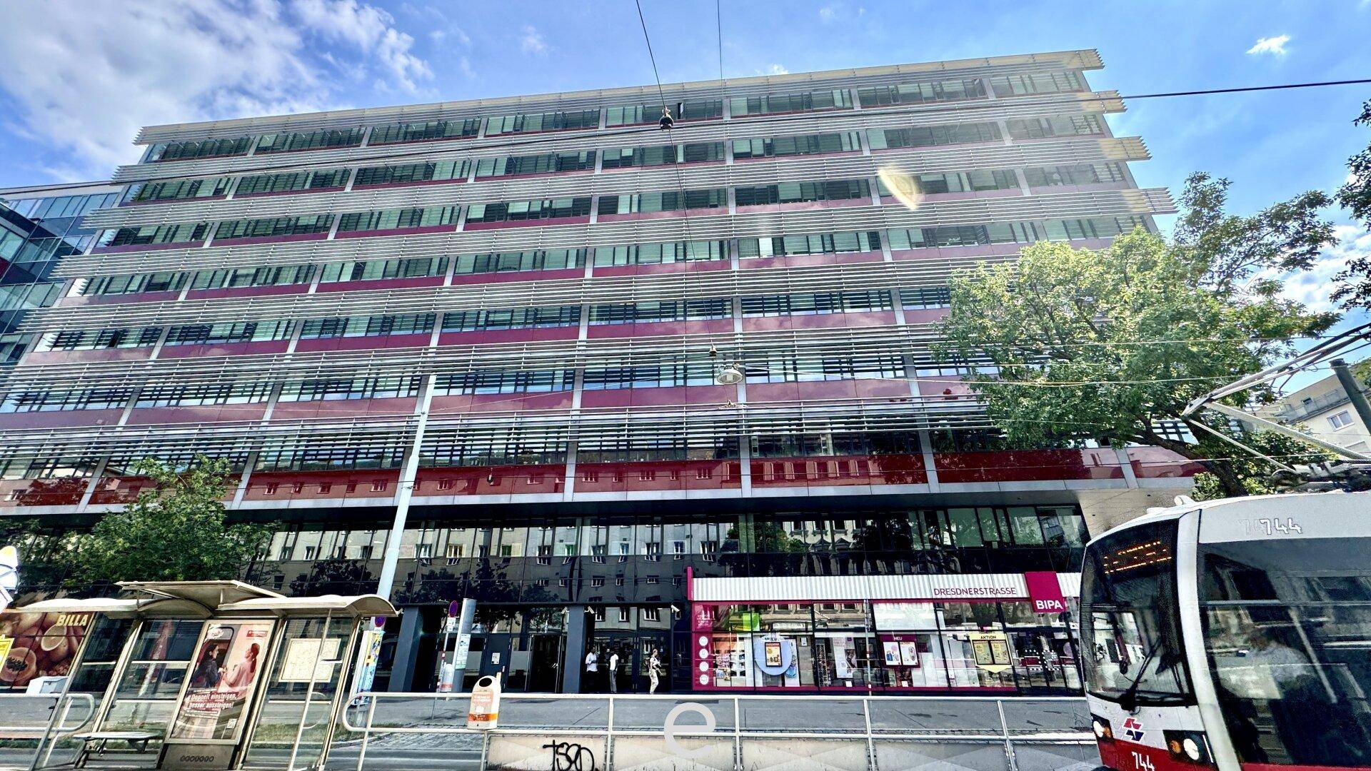 Großes Bürogebäude mit moderner Fassade und Geschäften im Erdgeschoss, an einer belebten Straße gelegen.