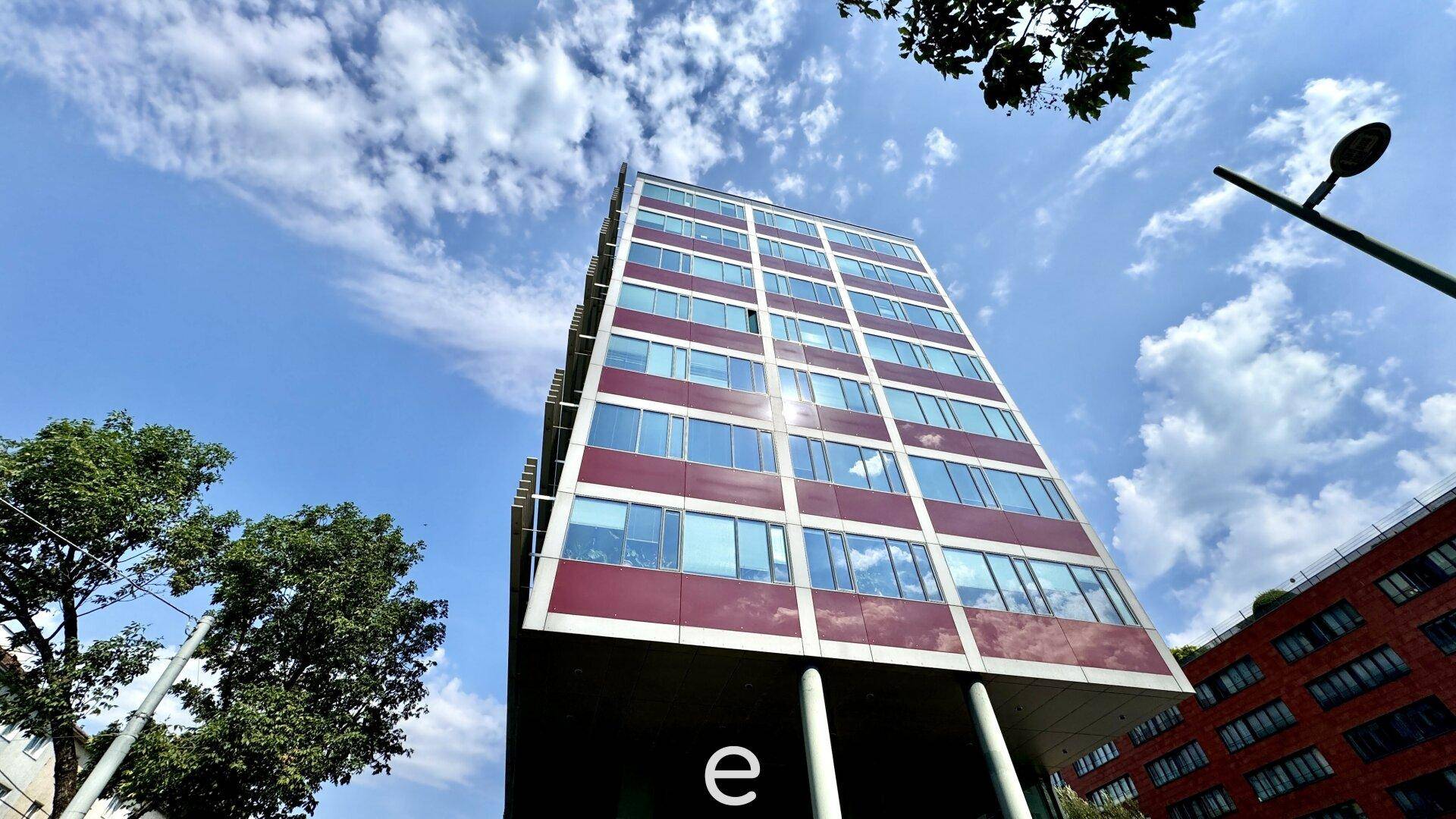 Hohes Bürogebäude mit markanter roter Fassade und vielen Fenstern unter blauem Himmel.