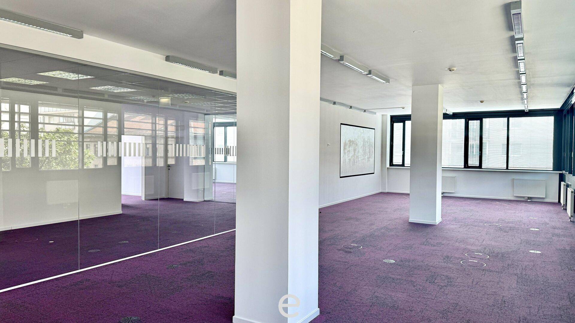 Geräumiges Büro mit lila Teppichboden, Säulen und Glaswänden, die den Raum flexibel gestalten.