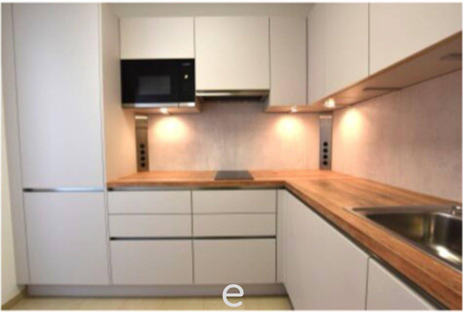 Moderne Einbauküche mit hellgrauen Fronten, Holzarbeitsplatte und integrierter Mikrowelle.