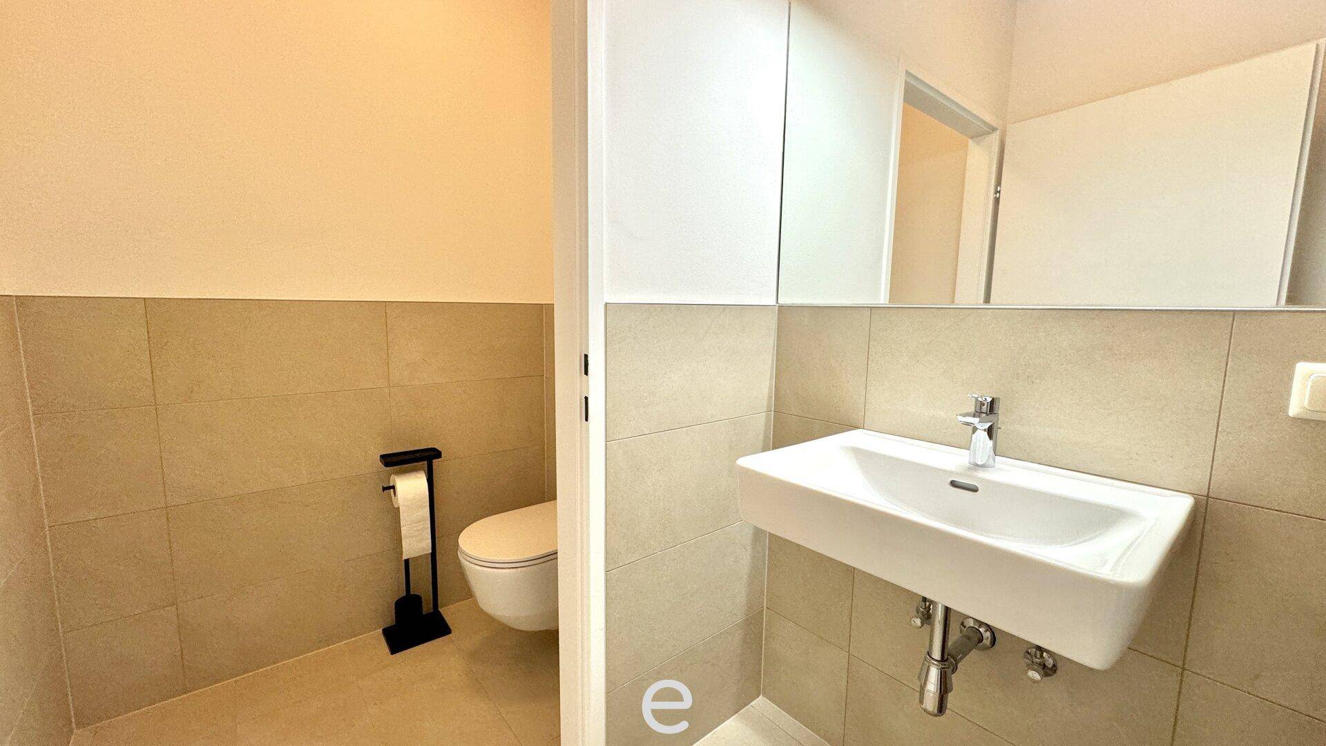 Modernes Gäste-WC mit beigefarbenen Fliesen, wandhängendem WC und rechteckigem Waschbecken.