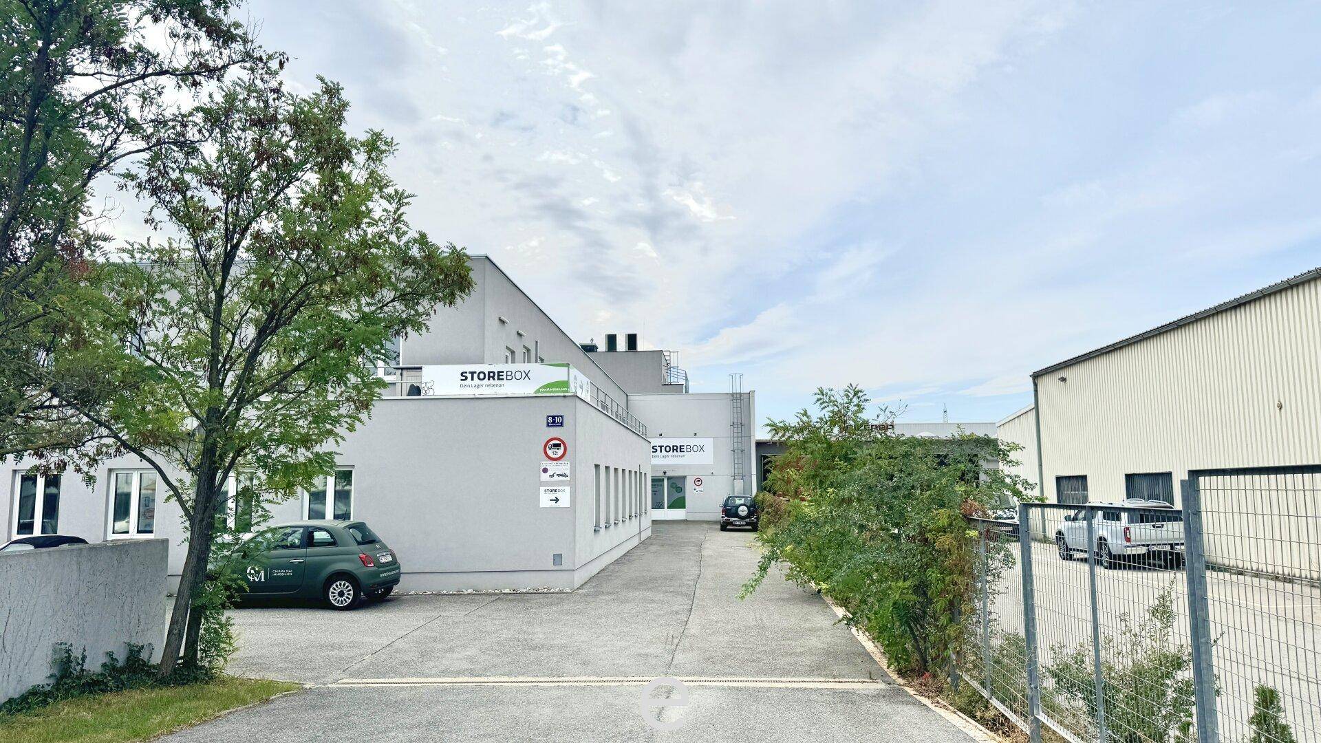 Außenansicht eines modernen Bürogebäudes mit Parkplätzen und umliegender Vegetation.