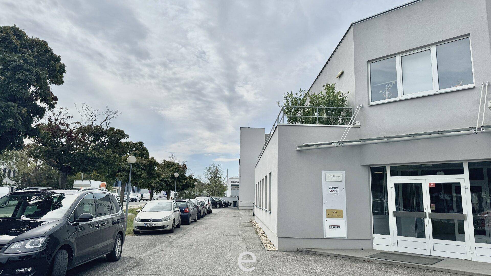 Modernes Bürogebäude mit grauer Fassade, großen Fenstern und einer Reihe geparkter Autos.