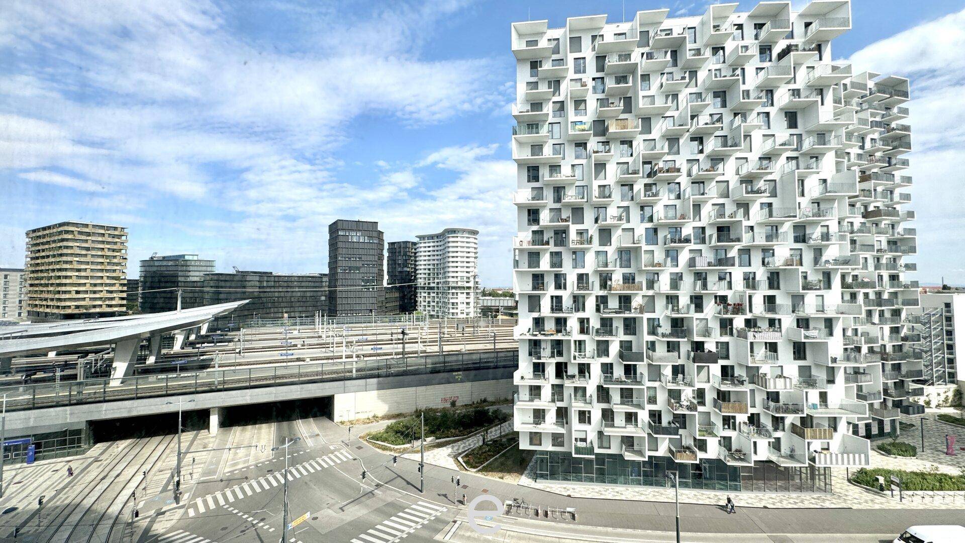 Weitläufige Stadtansicht mit modernen Gebäuden, Straßen und Bahngleisen unter blauem Himmel.