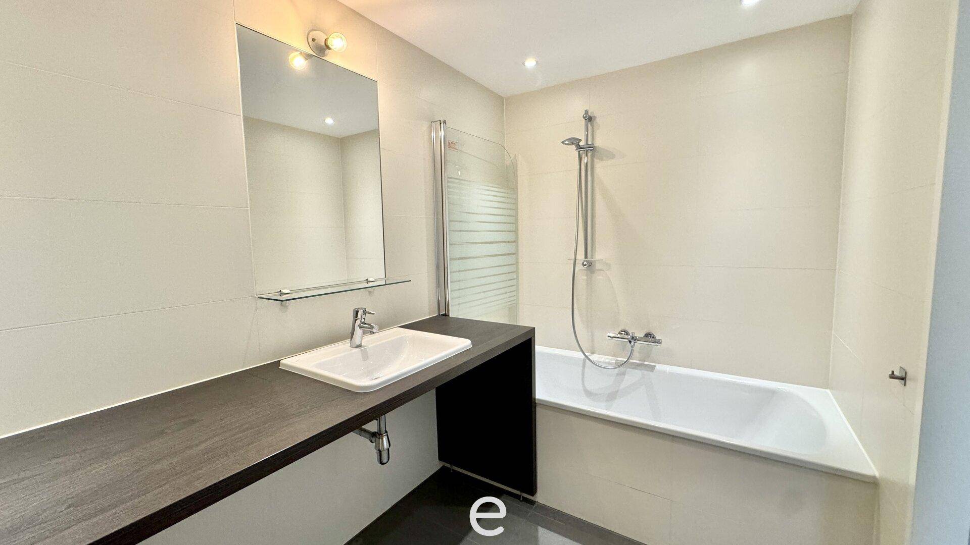Modernes Badezimmer mit Badewanne, Duschabtrennung, Waschtisch und großem Spiegel.