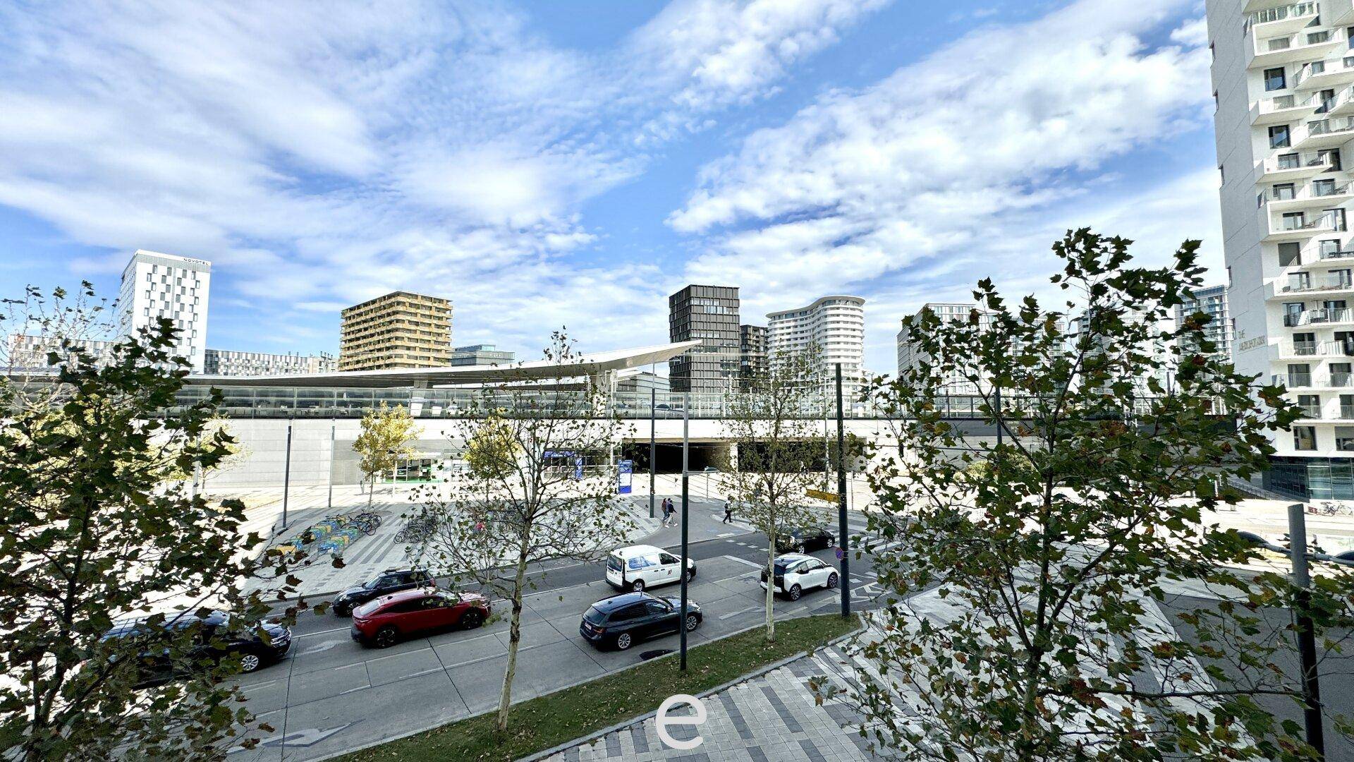 Blick auf eine belebte Stadtstraße mit modernen Gebäuden und viel Grün im Vordergrund.