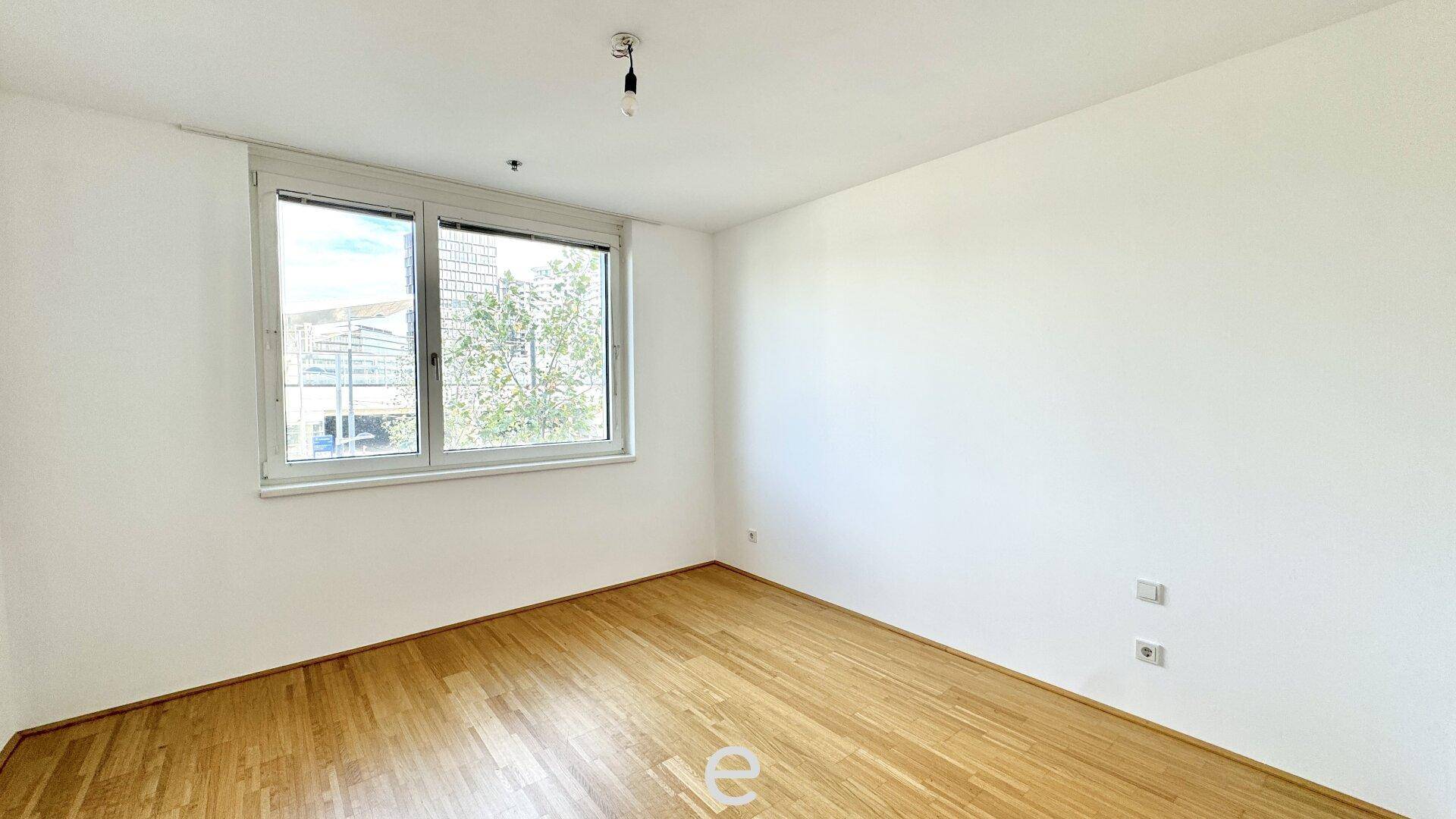 Helles Schlafzimmer mit Holzboden, weiß gestrichenen Wänden und einem großen Fenster.