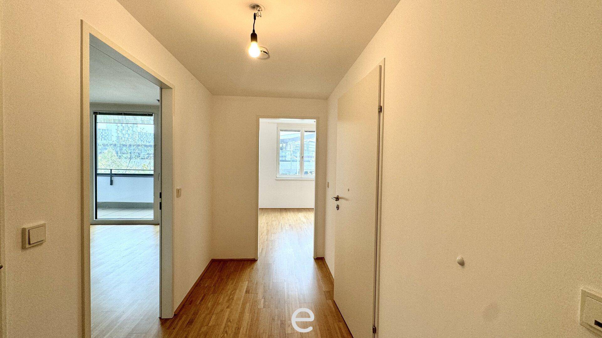Heller Flur mit Holzboden und weißen Wänden, der zu verschiedenen Räumen der Wohnung führt.