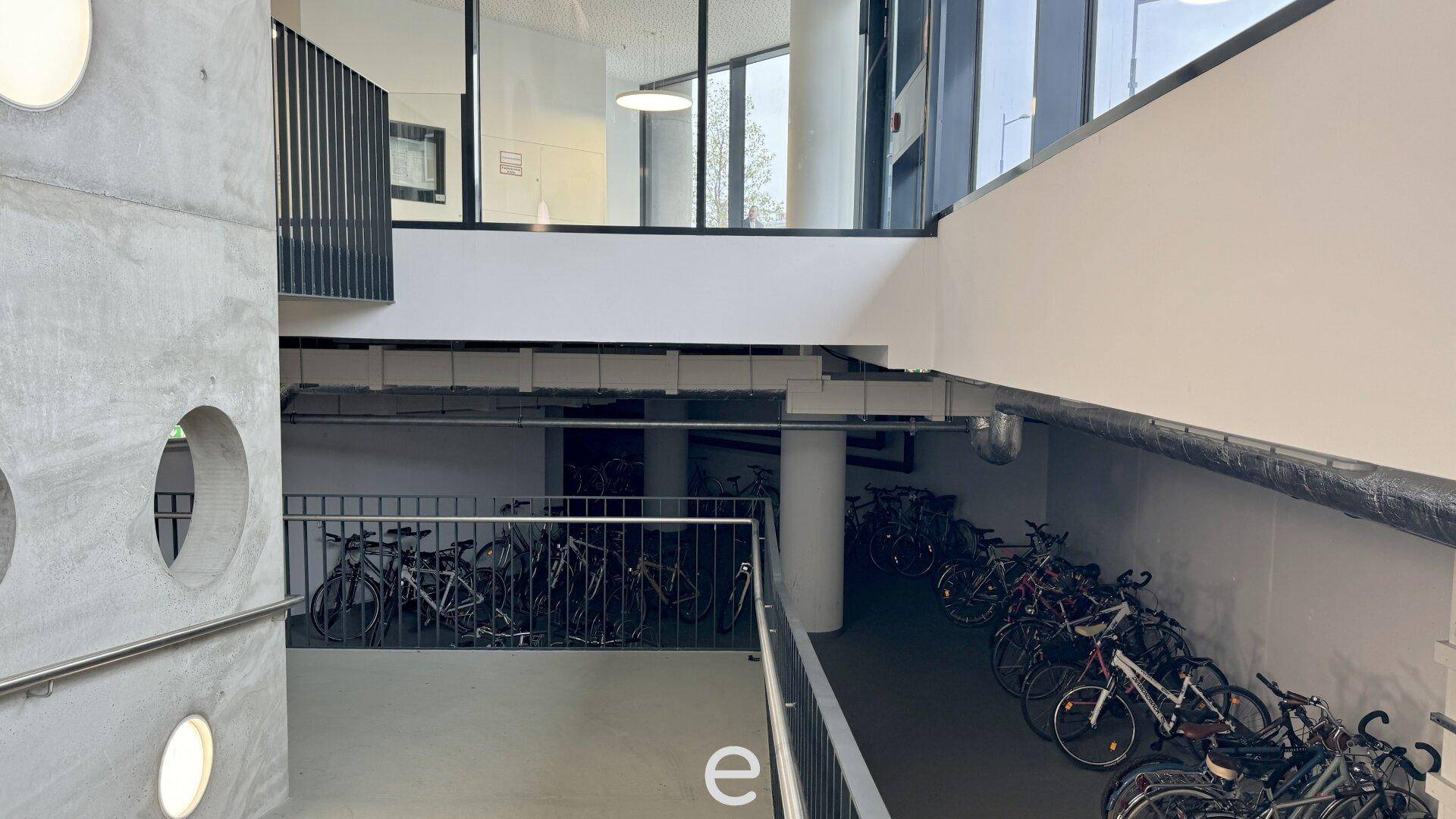 Geräumiger Fahrradraum im Untergeschoss mit vielen abgestellten Fahrrädern und Betonwänden.