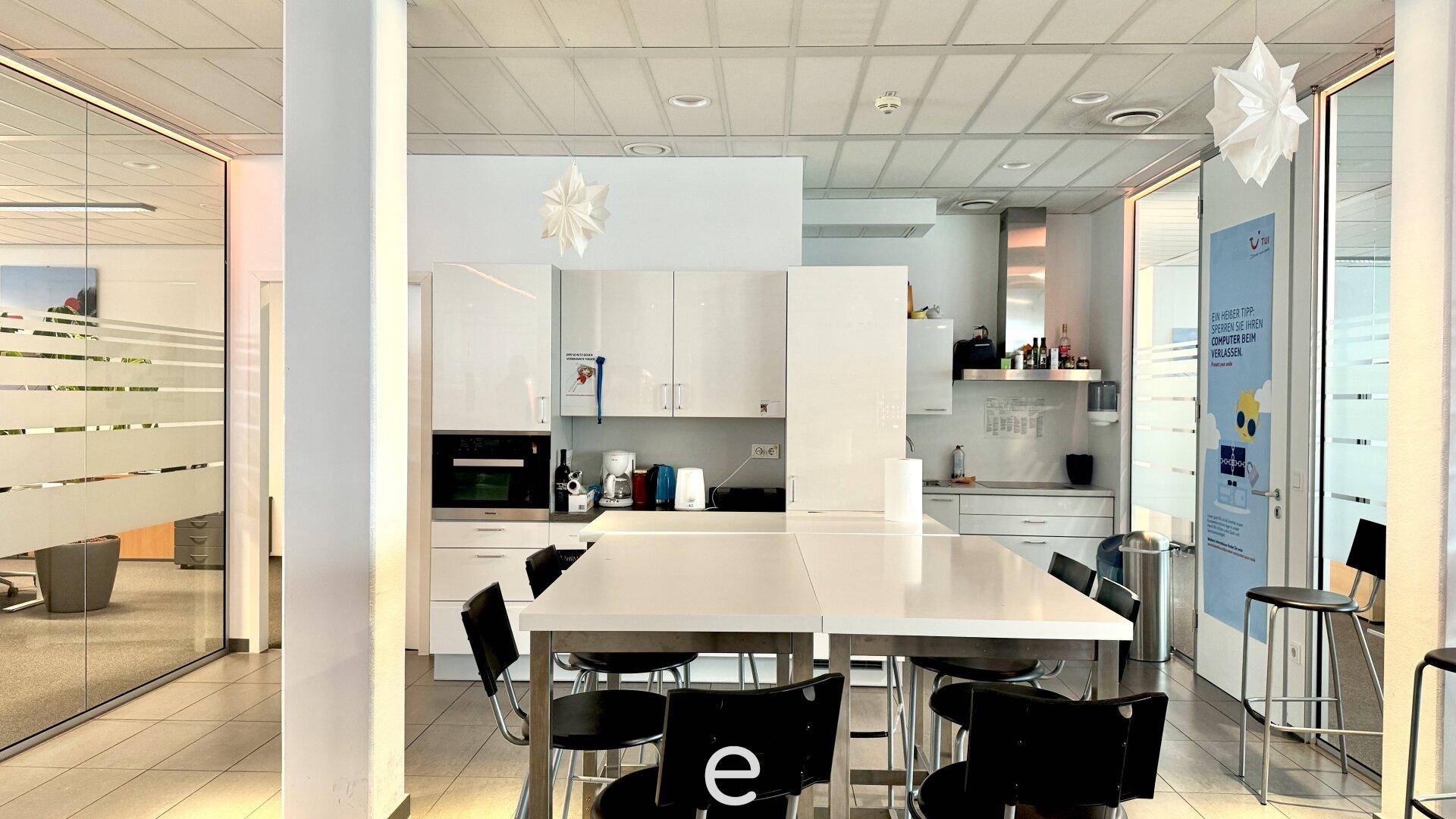 Moderne Büroküche mit weißen Hochglanzschränken, Esstisch und schwarzen Stühlen.