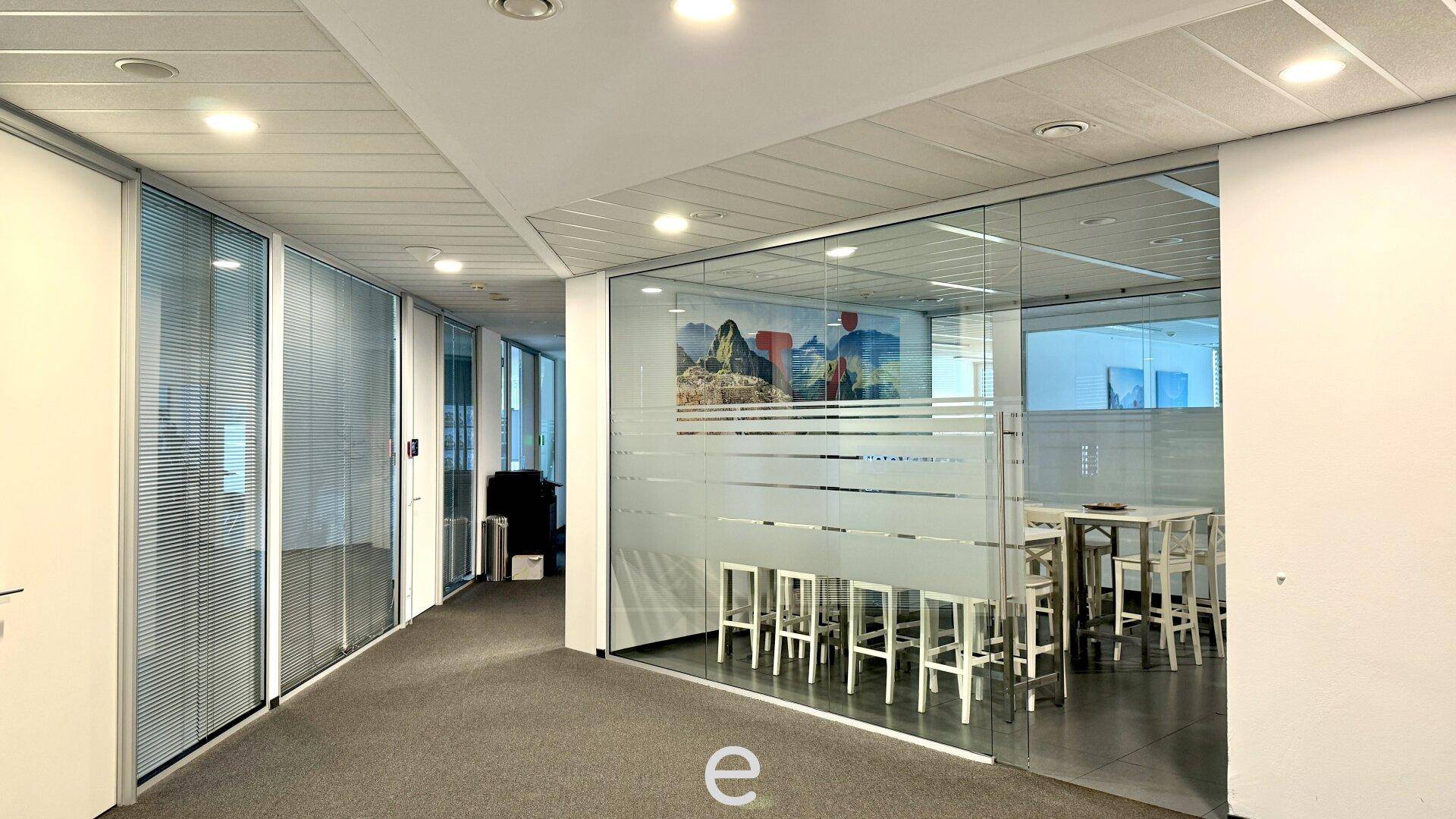 Heller Büroflur mit Glastrennwänden, die zu einem Besprechungsraum führen.