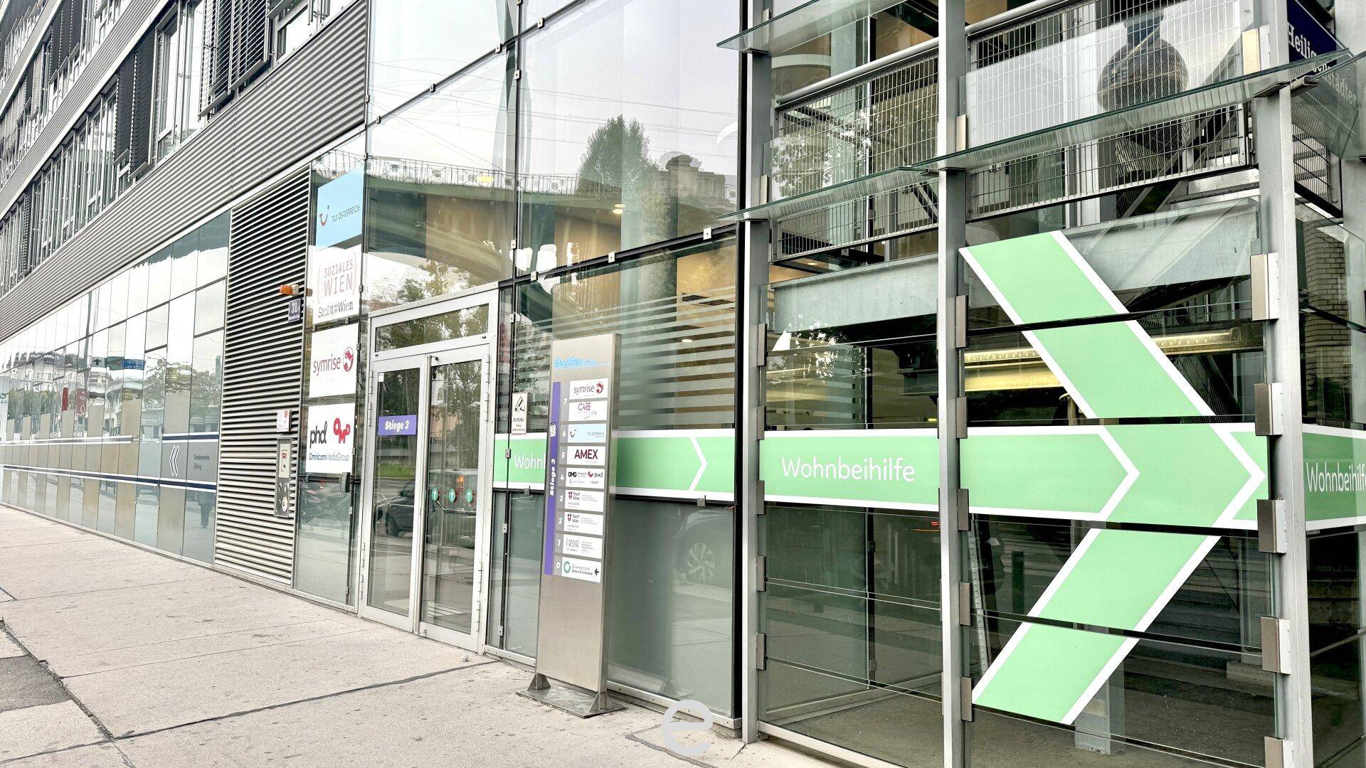 Eingangsbereich eines modernen Bürogebäudes mit Glasfassade und grünen Wegweisern.