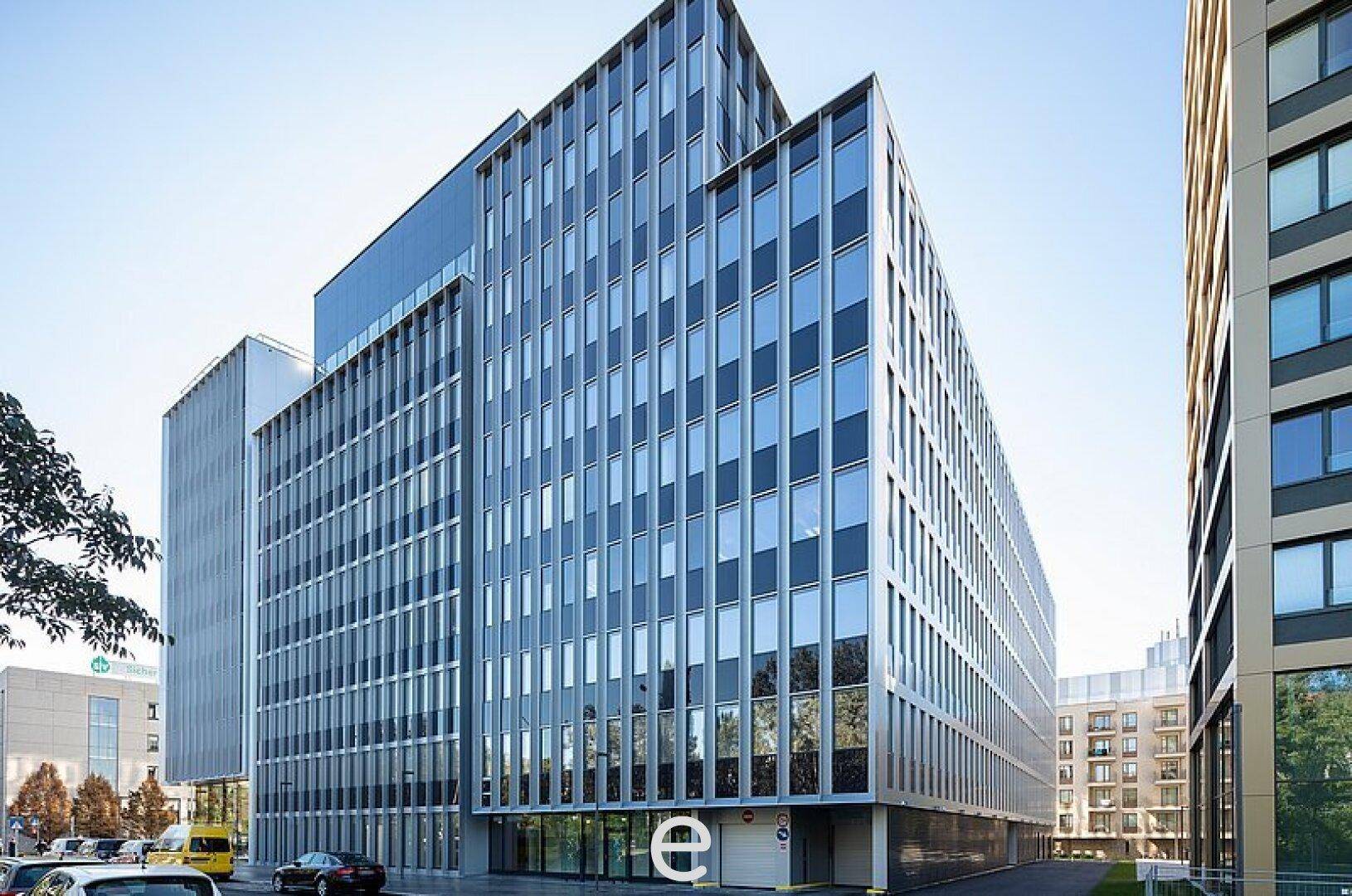Modernes Bürogebäude mit Glasfassade und klaren Linien unter blauem Himmel in einer städtischen Umgebung.