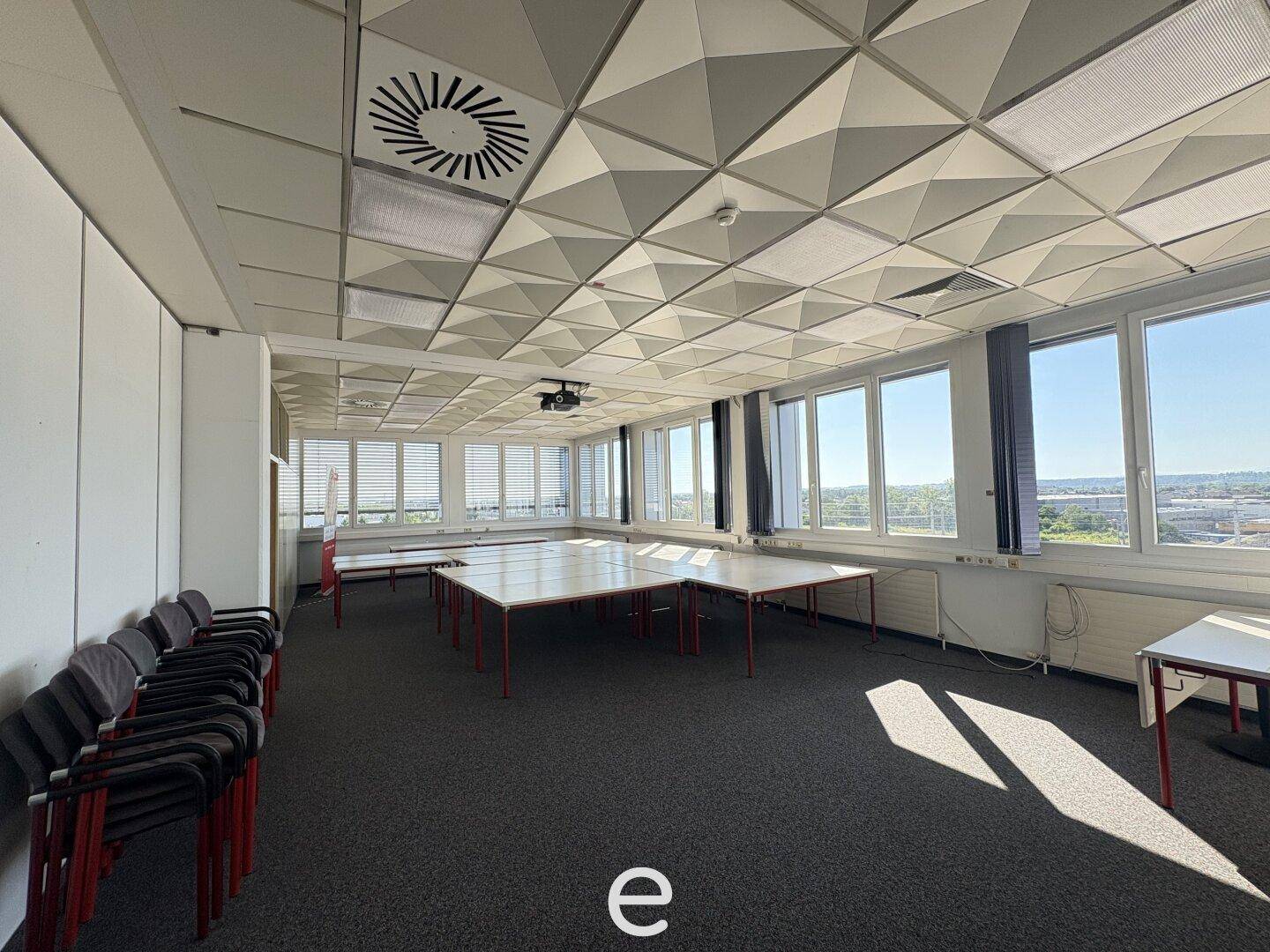 Großer Konferenzraum mit vielen Fenstern, modularen Tischen und einer abgehängten Decke.