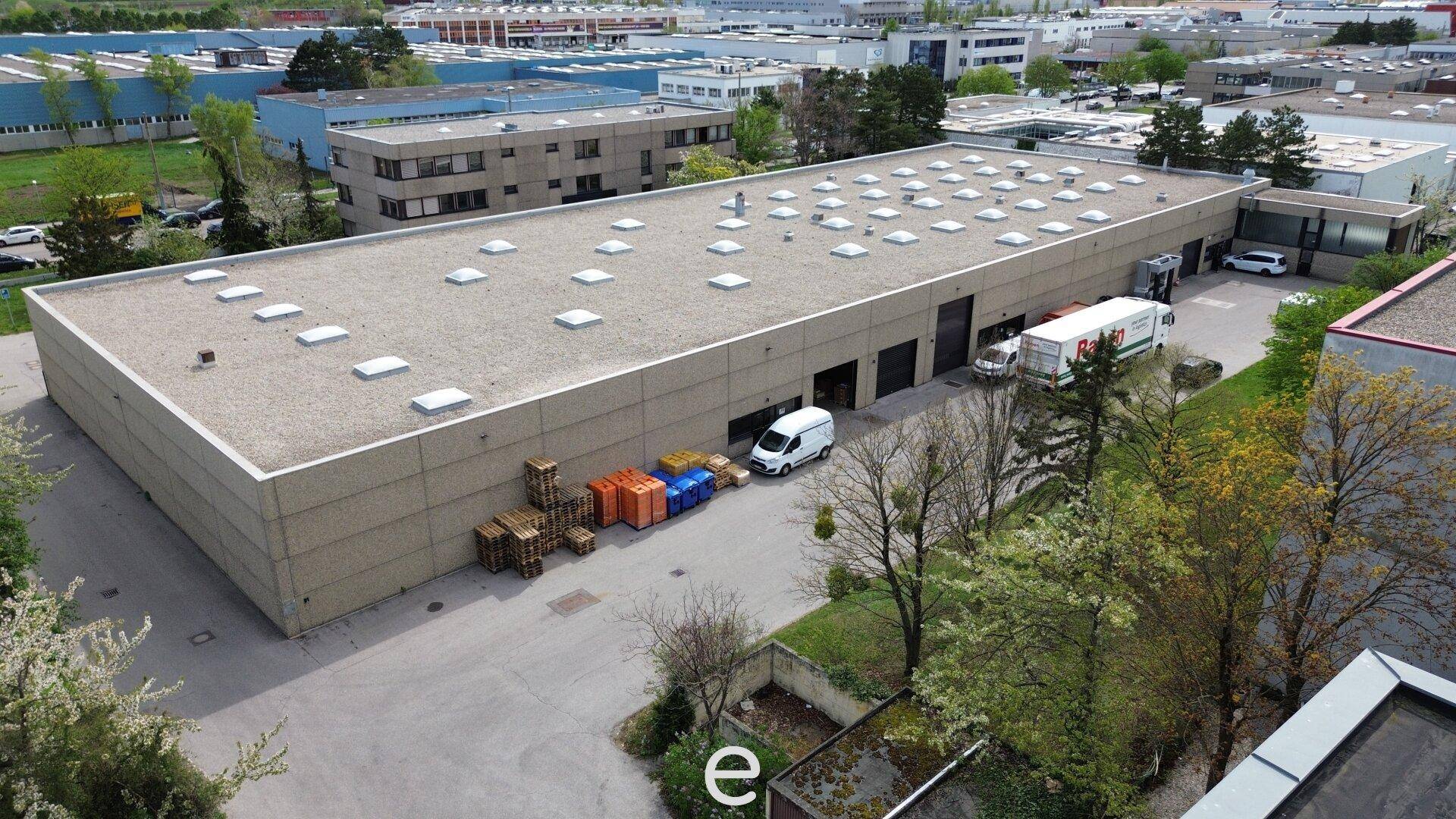 Luftaufnahme der großen Lagerhalle mit Flachdach, Oberlichtern und Laderampen in einem Gewerbegebiet.