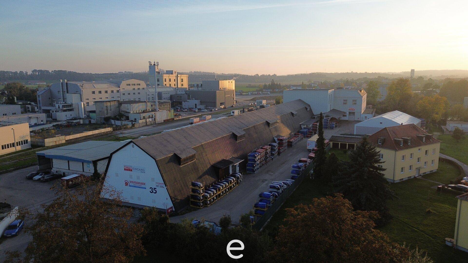 Luftaufnahme eines weitläufigen Industriekomplexes bei Sonnenuntergang mit mehreren Gebäuden und Parkplätzen.