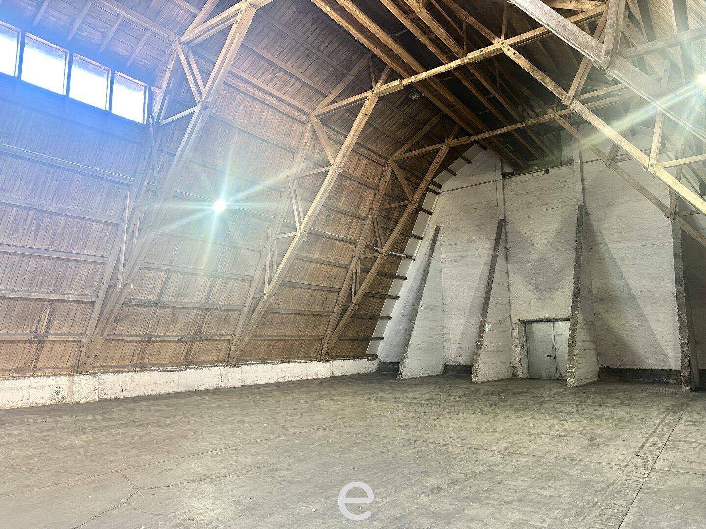 Weitläufige Lagerhalle mit beeindruckender Holzrahmenkonstruktion und robustem Betonboden, ideal für Lagerung.