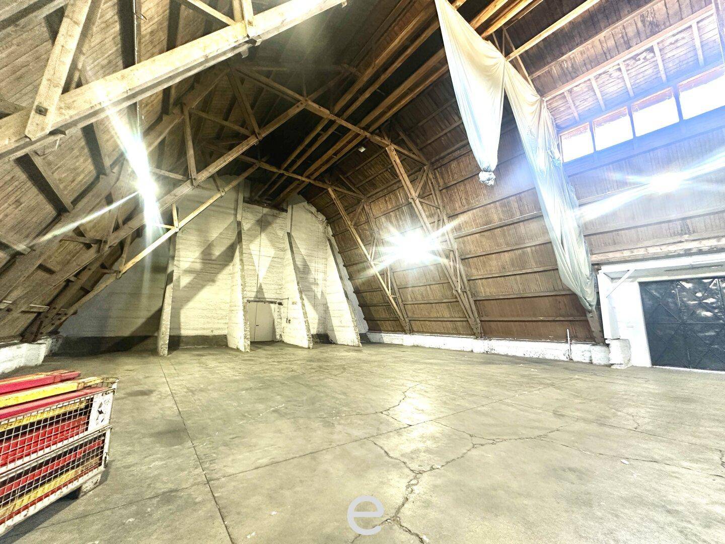 Innenansicht einer großen Lagerhalle mit markanter Holzkonstruktion, Betonboden und viel natürlichem Licht.