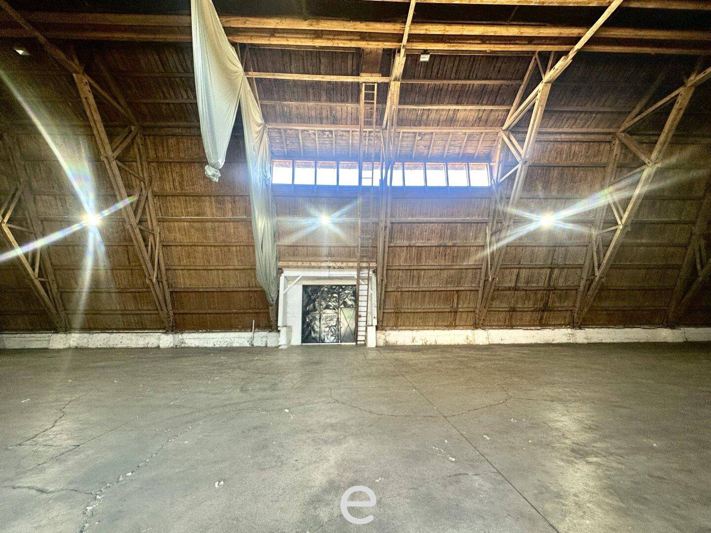 Große Lagerhalle mit Rolltor, hoher Holzdecke und Oberlichtern, die für natürliche Beleuchtung sorgen.