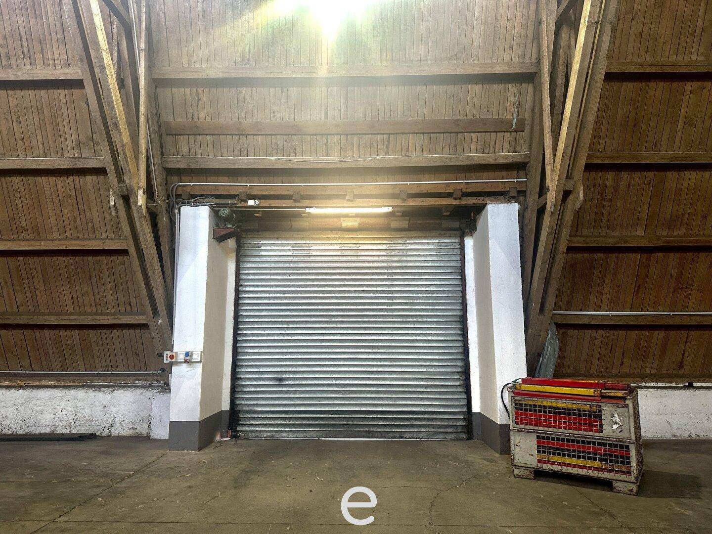 Großer Rolltor-Eingang in einer Lagerhalle mit hoher Holzkonstruktion und Betonboden.