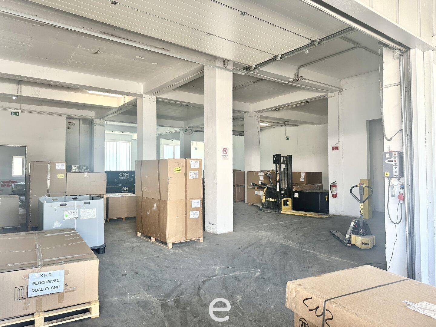 Lagerhalle mit gestapelten Kartons, Paletten und Gabelstaplern, bereit für Logistikoperationen.