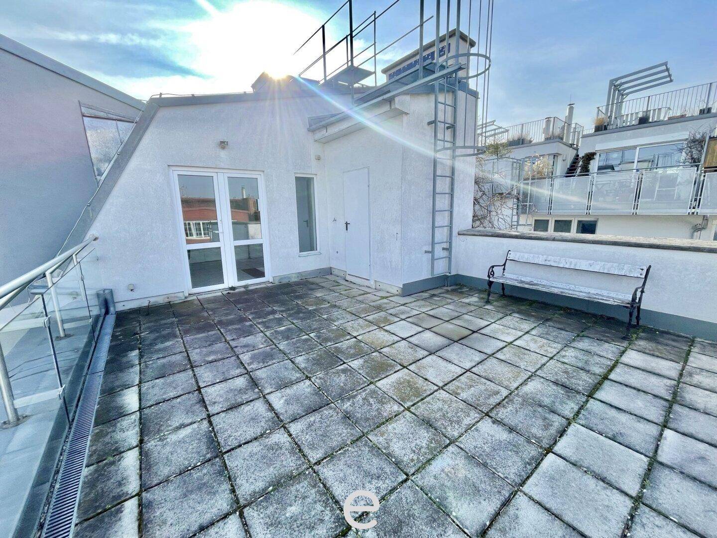 Sonniger Terrassenbereich mit Fliesenboden, Sitzbank und Zugang zum Dachgeschoss.