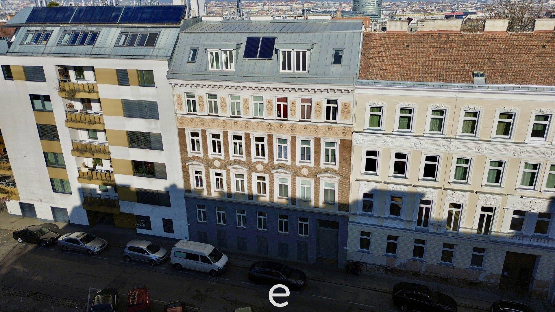 Ansicht der Gebäudefassade mit verschiedenen Architekturstilen und Solarpaneelen auf dem Dach.