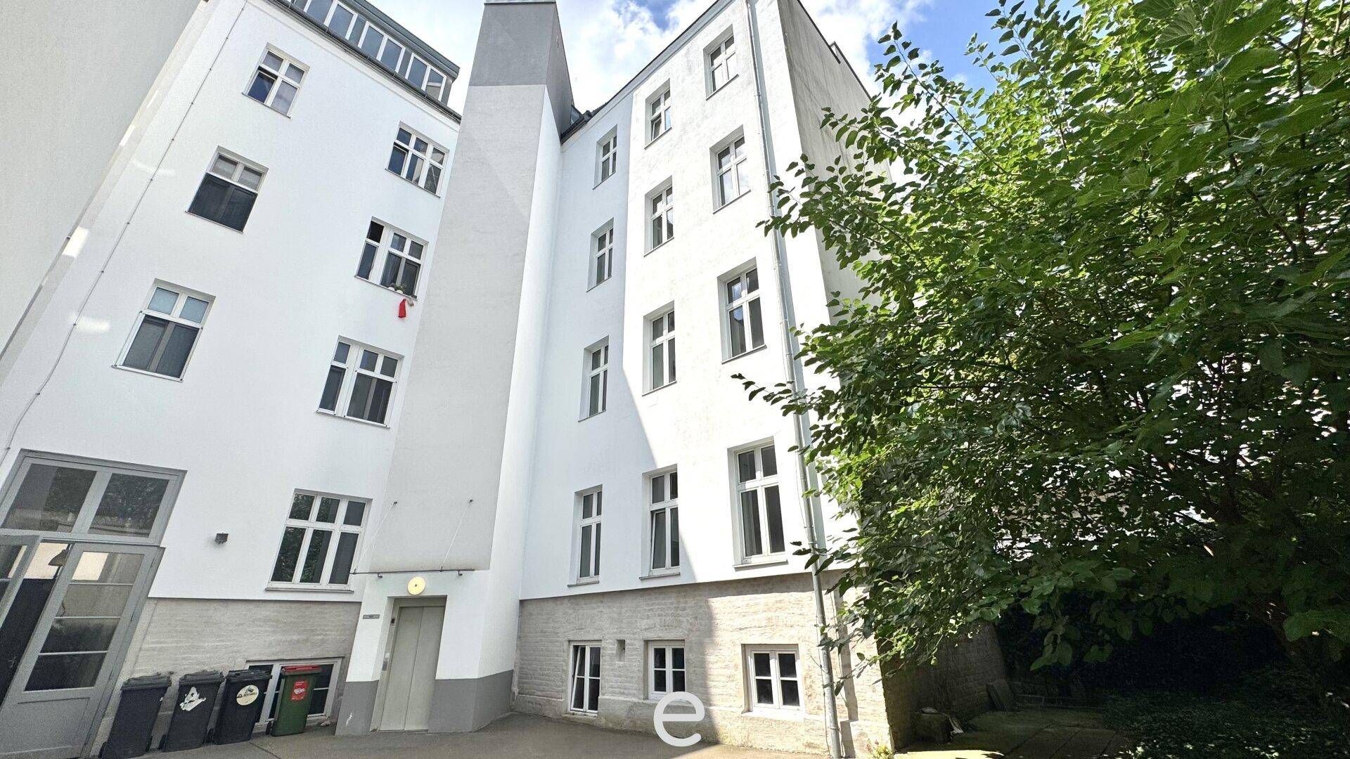 Außenansicht eines weißen Gebäudes mit schmalem Durchgang und Grünbereich im Innenhof.