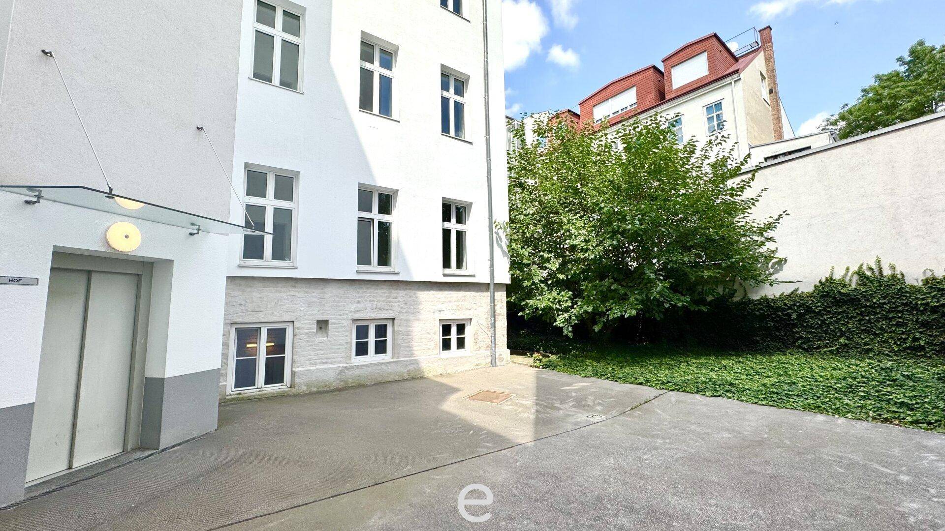 Außenbereich eines Gebäudes mit einem Aufzug am Eingang und einer kleinen Grünfläche daneben.