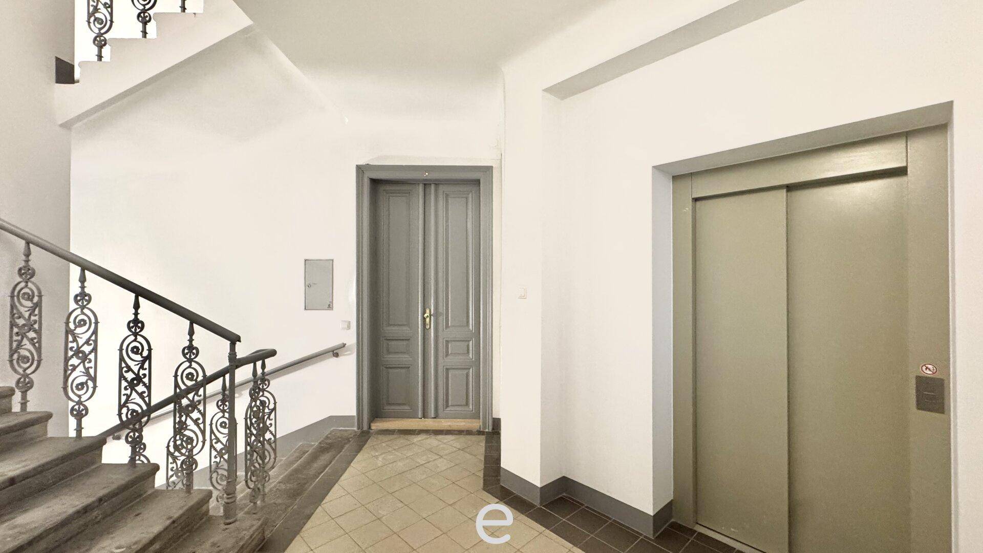 Eingangsbereich mit einer eleganten Treppe, schmiedeeisernem Geländer und einem Aufzug.